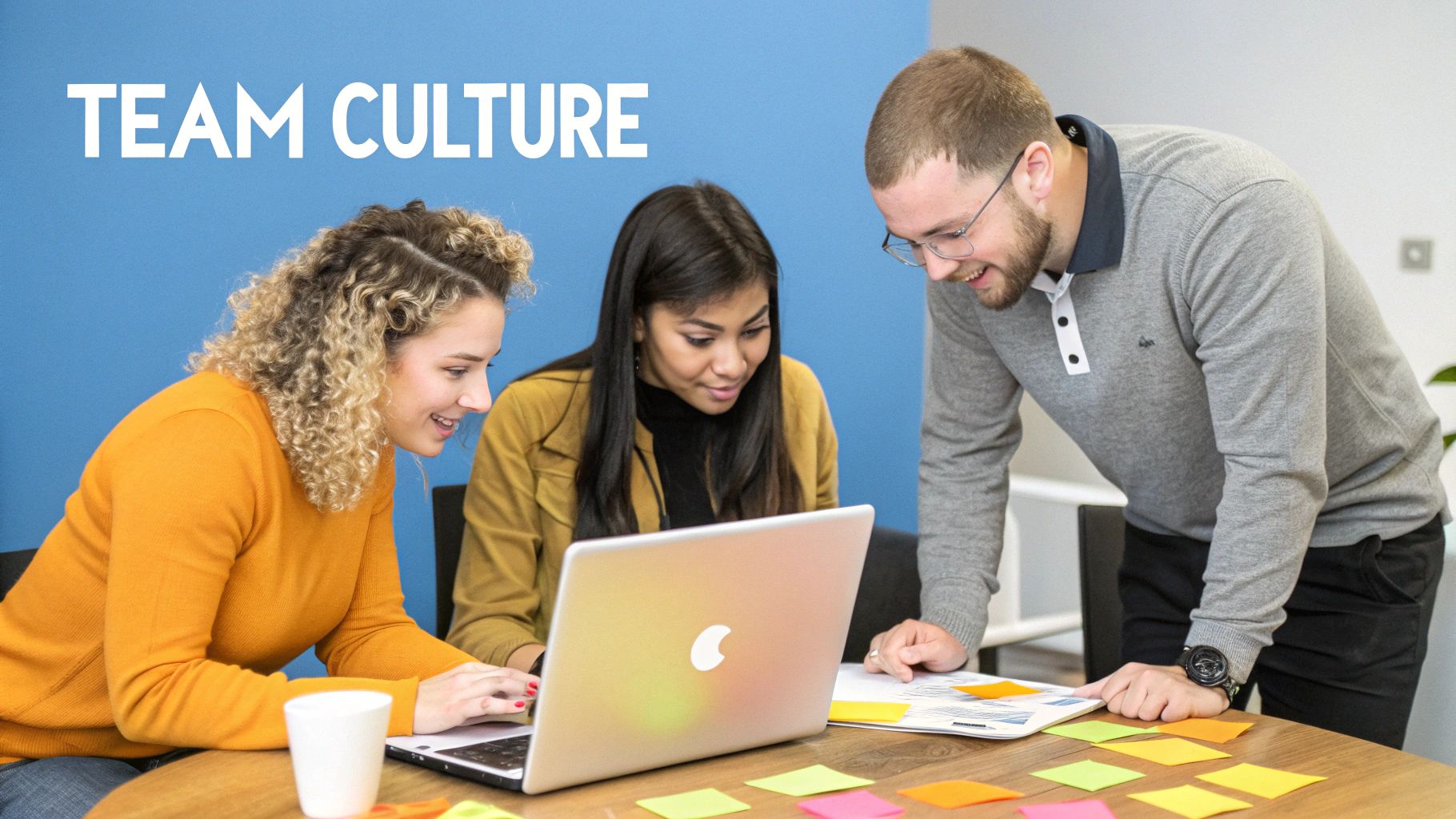 Three diverse colleagues collaborating around a laptop and sticky notes, representing strong team culture.