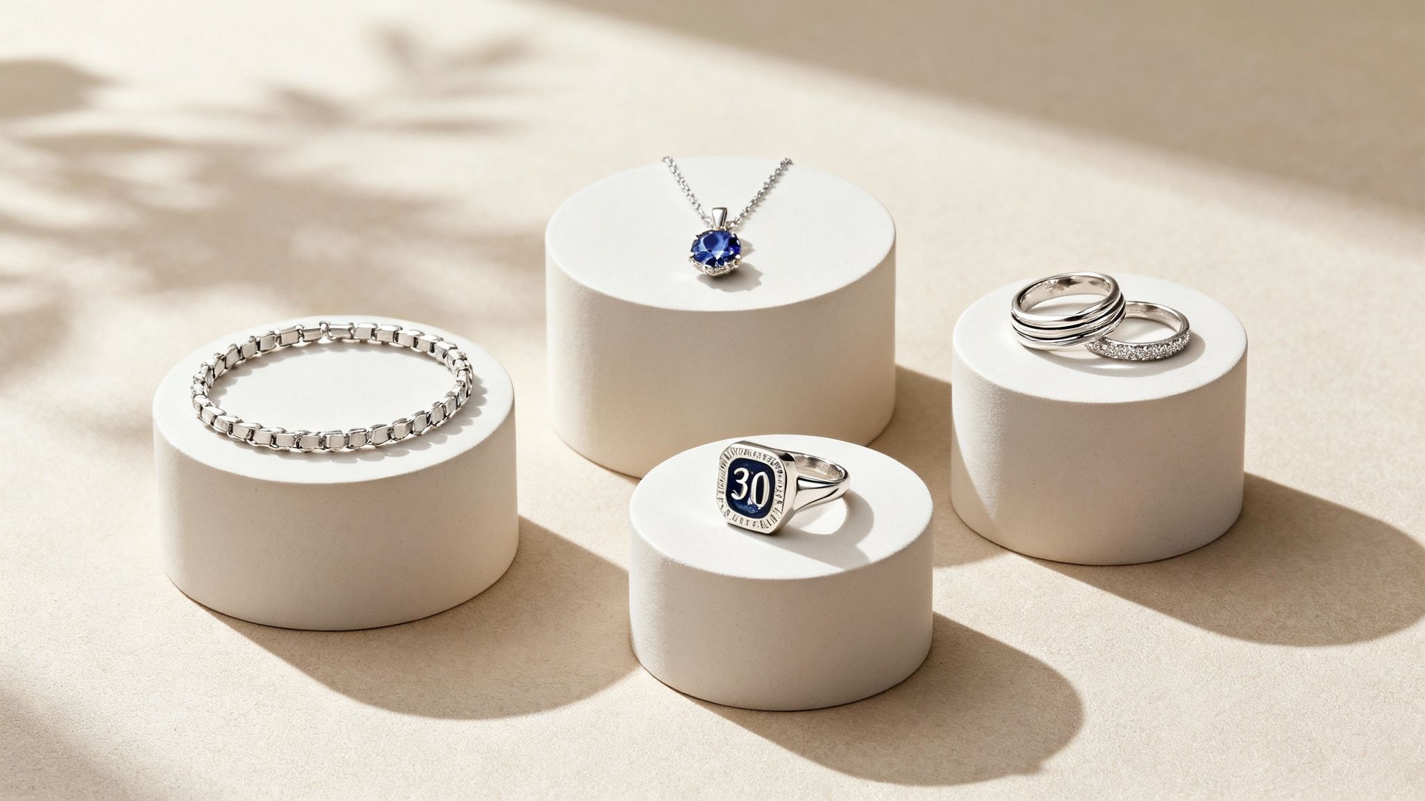Elegant silver jewelry display featuring necklace, bracelet, rings and number thirty signet ring on white pedestals