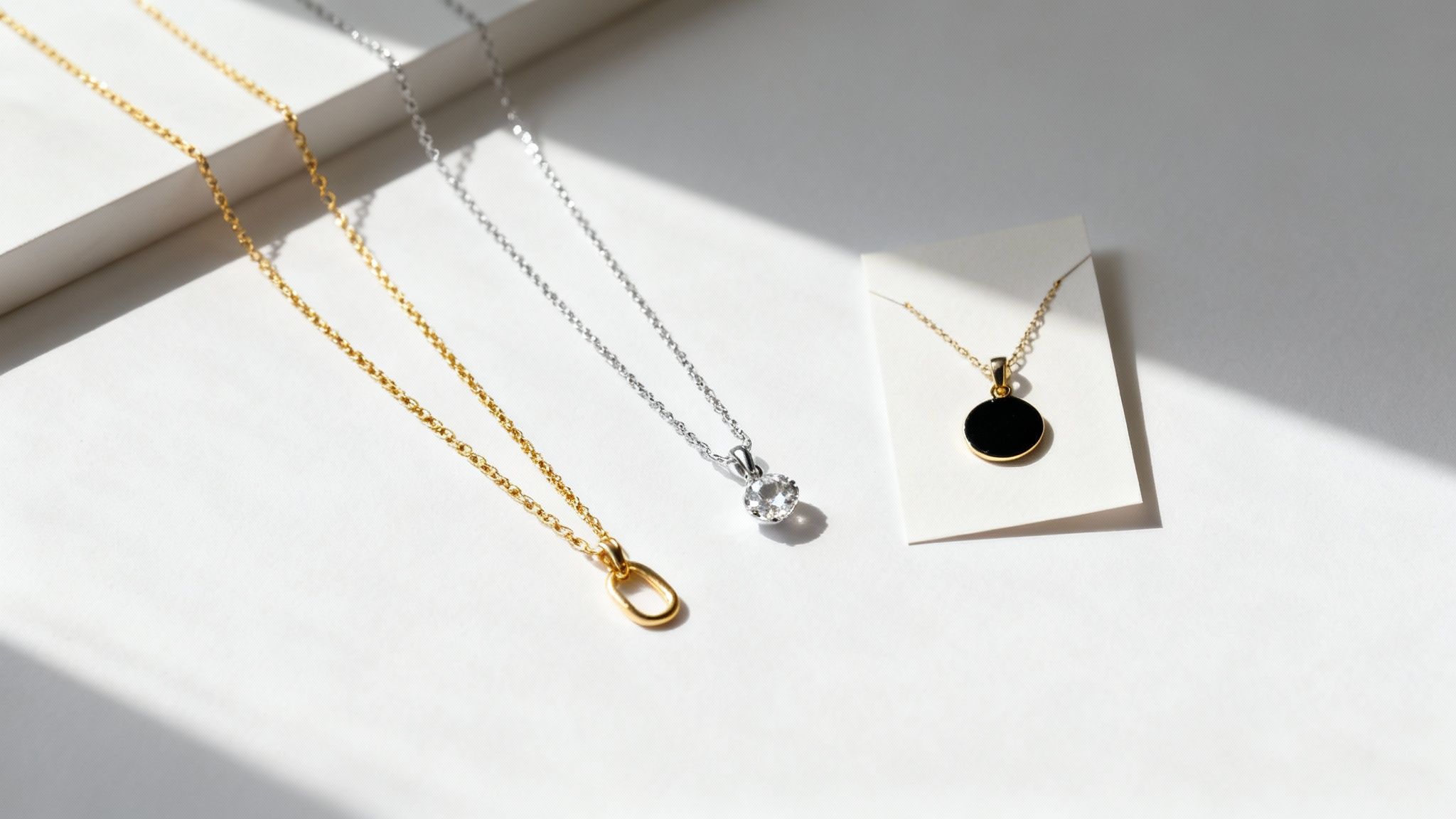 Three delicate gold and silver pendant necklaces displayed on white surface with natural lighting