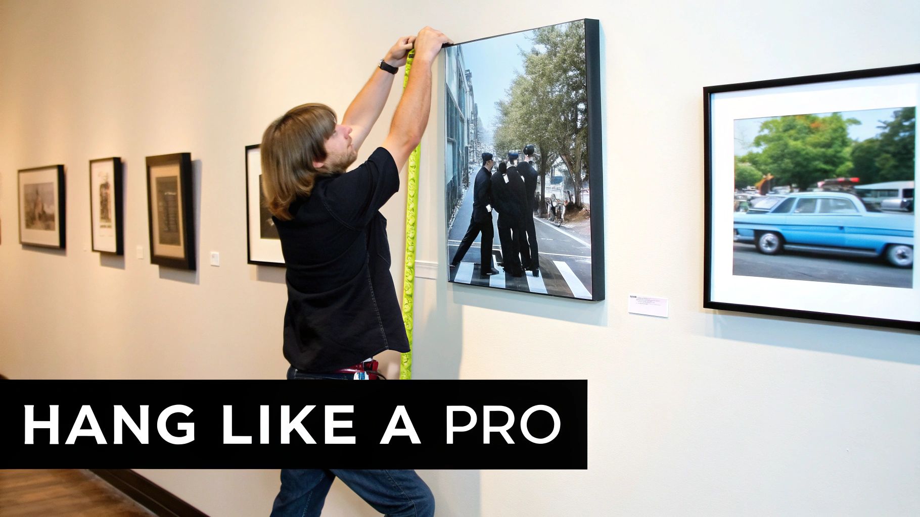 A person precisely measures while hanging a large framed print of men in suits on a gallery wall.