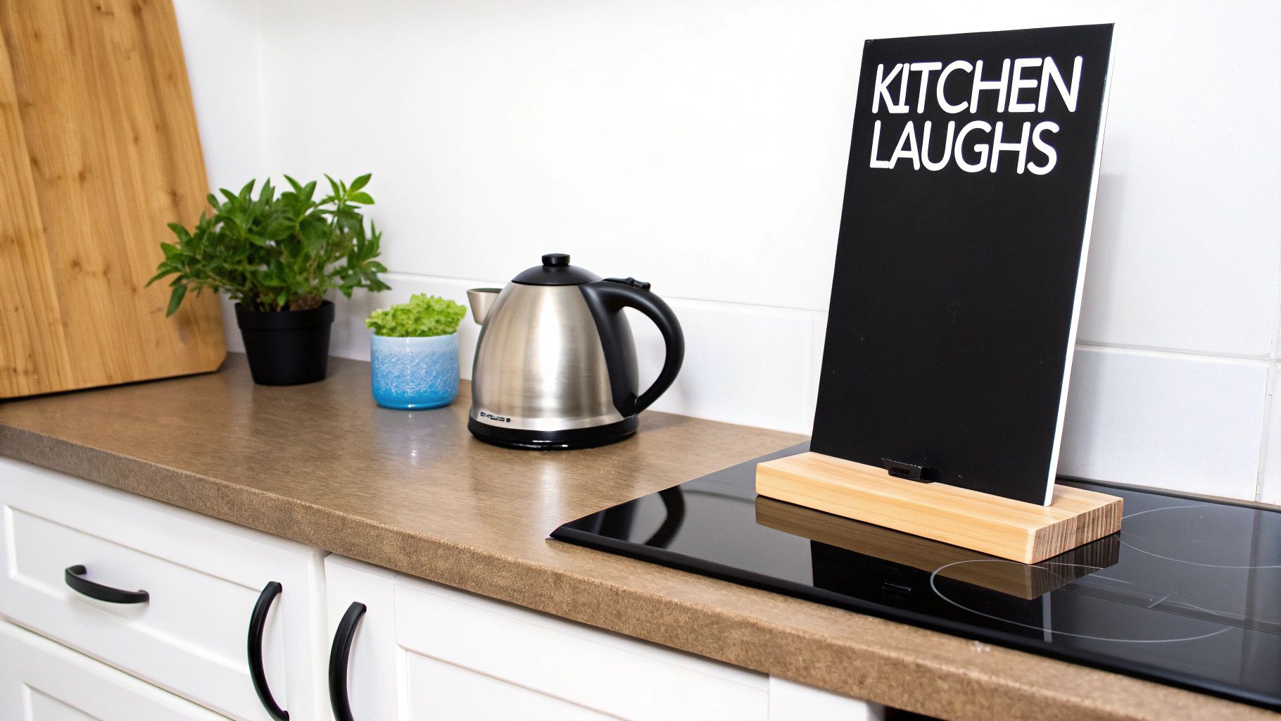 Clean kitchen featuring a stainless steel kettle, green plants, and a fun 'Kitchen Laughs' sign.