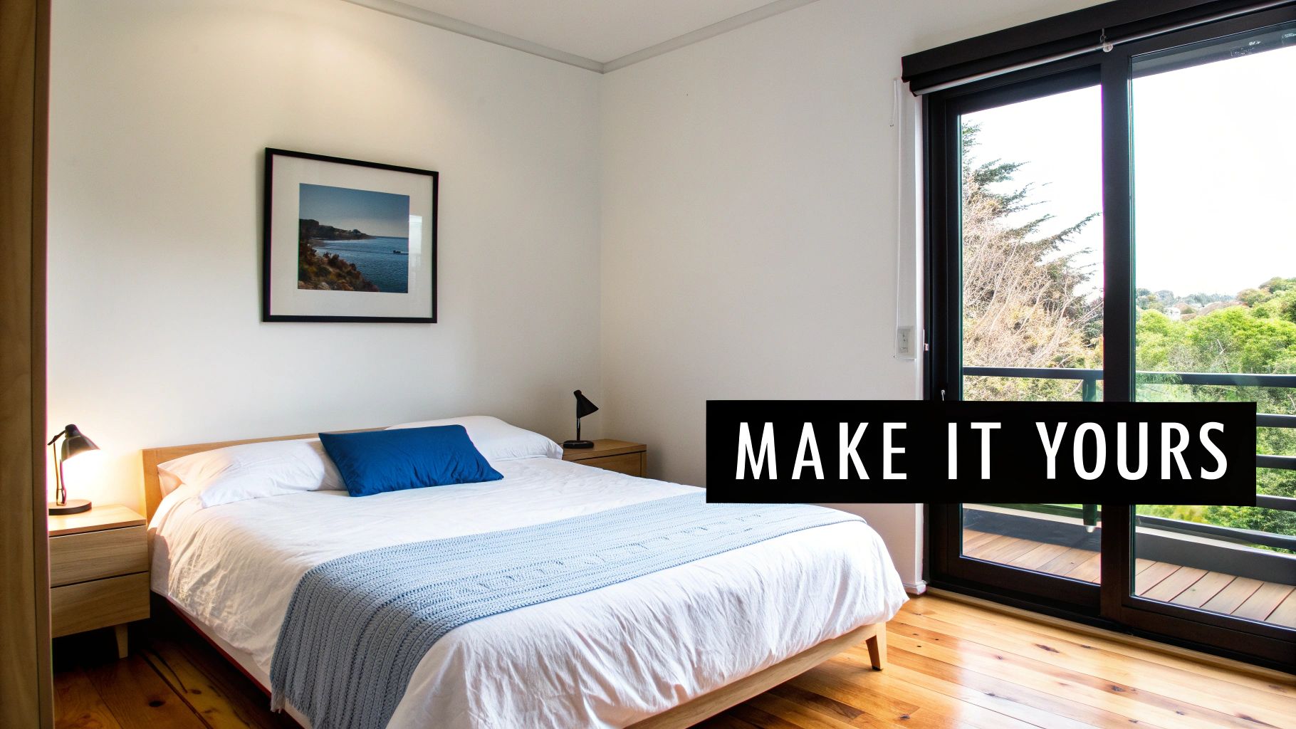 Modern minimalist bedroom with wooden bed, blue accents, framed coastal print, and large window overlooking greenery