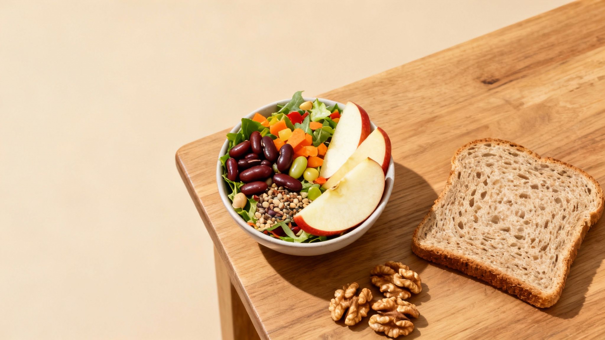 A healthy meal on a wooden table, featuring a colorful salad bowl, sliced apple, whole wheat bread, and walnuts.