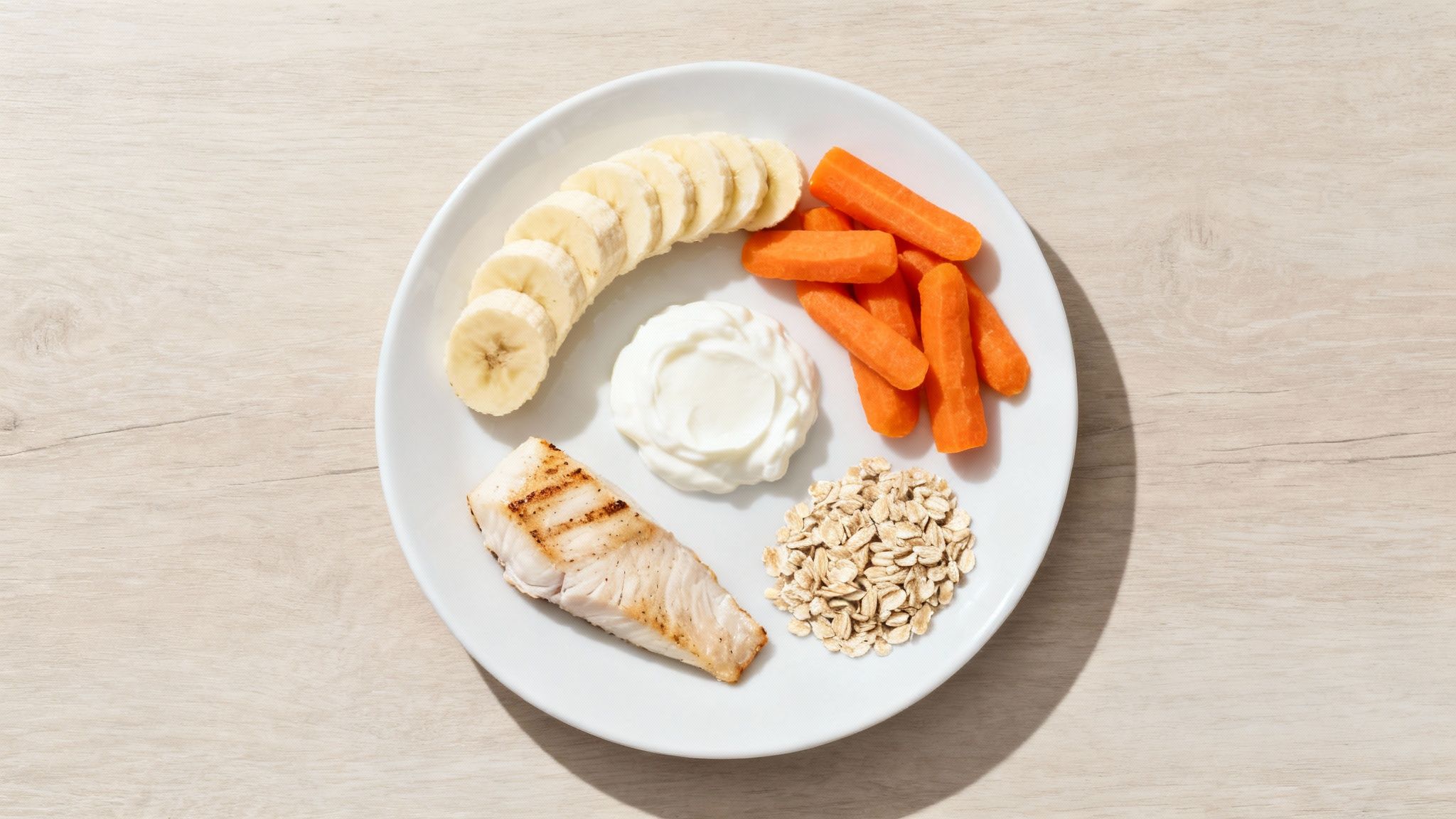 A colorful array of gut-friendly foods, including leafy greens, lean chicken, bananas, and oatmeal, arranged neatly on a wooden table.
