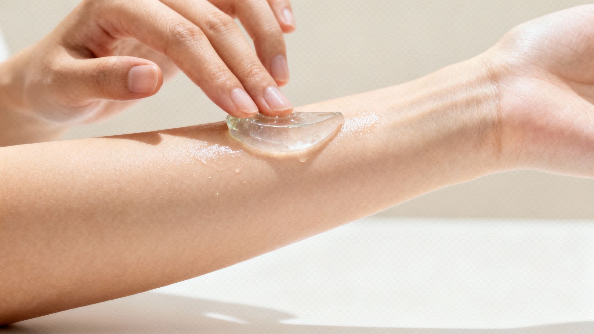A close-up of a hand applying a clear aloe vera gel onto a person's moisturized arm.