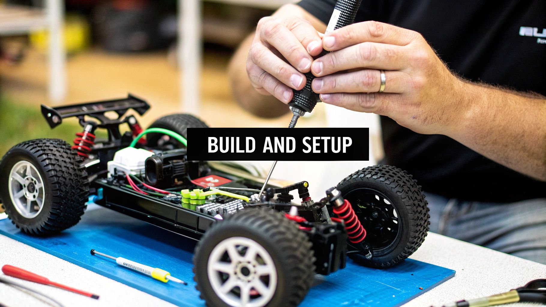 Close-up of hands building a remote control (RC) car kit, with tools and components on a blue mat.