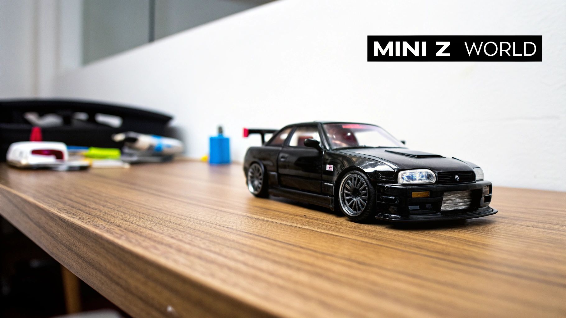 A black Kyosho Mini-Z model car, resembling a Nissan Skyline, sits on a wooden desk.