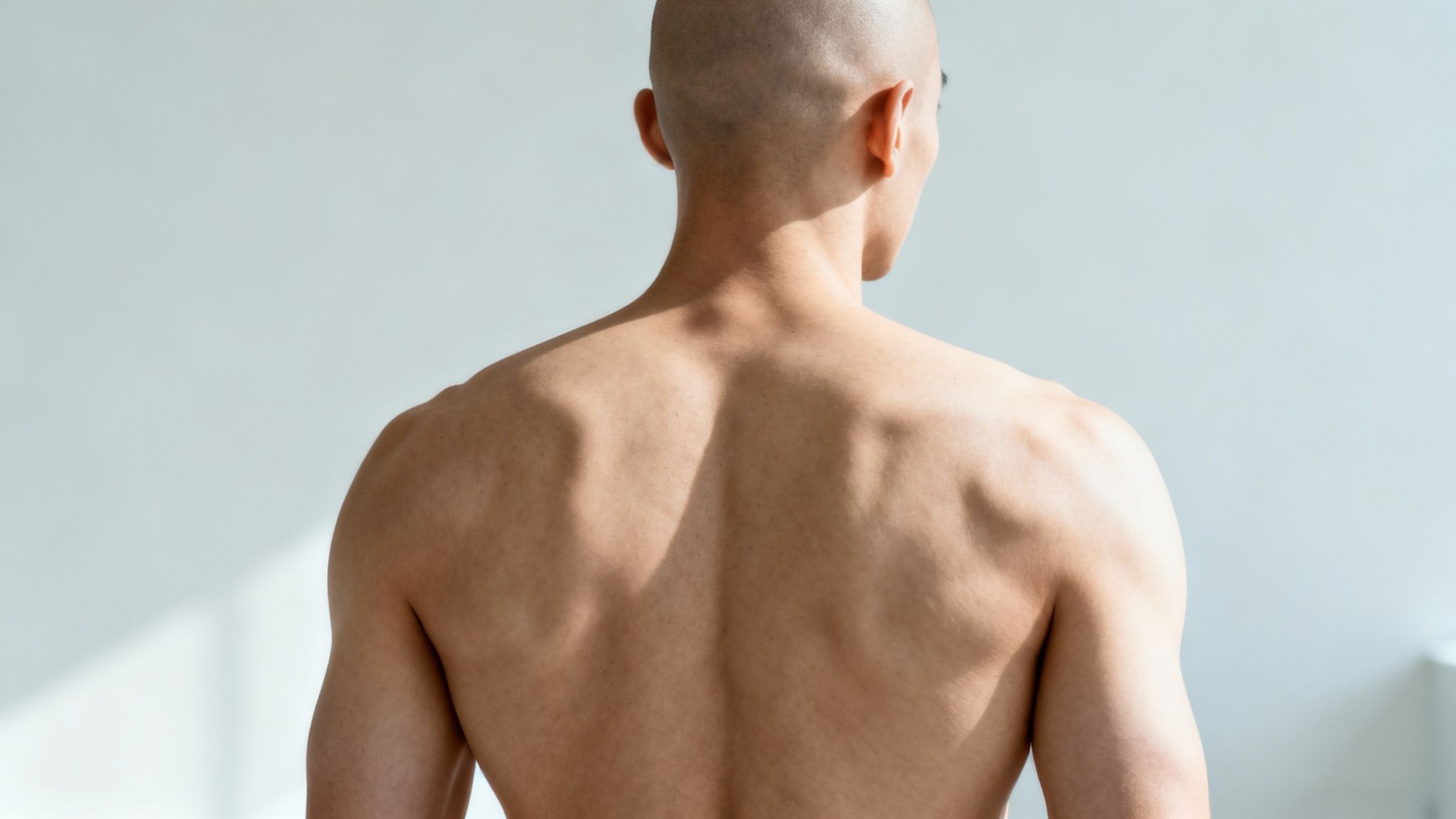 Ghidul complet: epilare definitiva barbati și cum să alegi clinica ideală 2 Epilare definitiva barbati Spatele unui bărbat chel, musculos, fără cămașă, privitor la distanță, pe un fundal deschis.