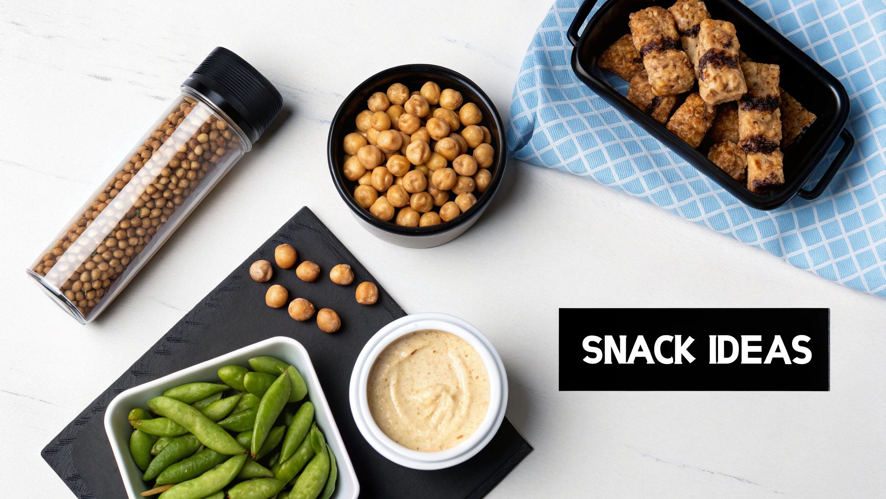 A variety of healthy snack ideas including roasted chickpeas, edamame, and dessert bars, on a white table.