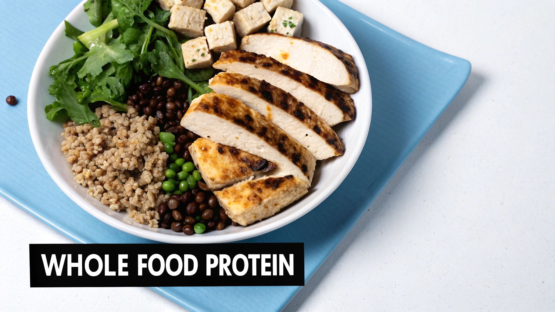 A healthy bowl with grilled chicken, tofu, greens, lentils, peas, and grains on a blue mat.