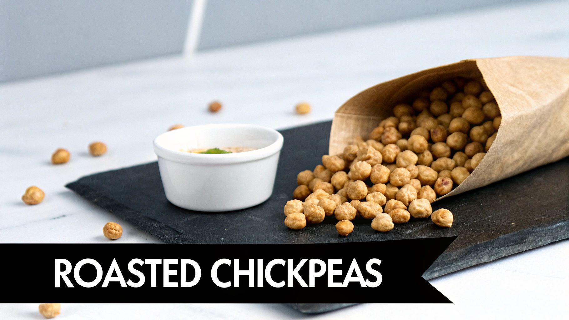 A brown paper bag filled with roasted chickpeas spilling onto a dark board, next to a dip.