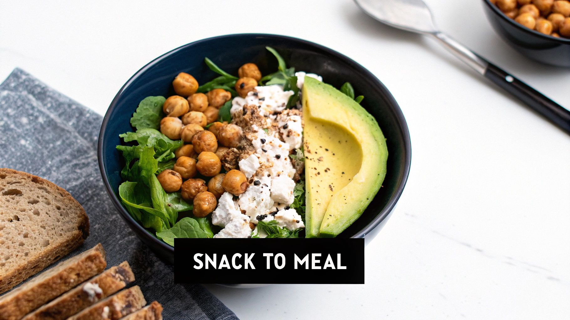 A vibrant bowl filled with chickpeas, fresh avocado, crumbled feta cheese, and leafy greens.