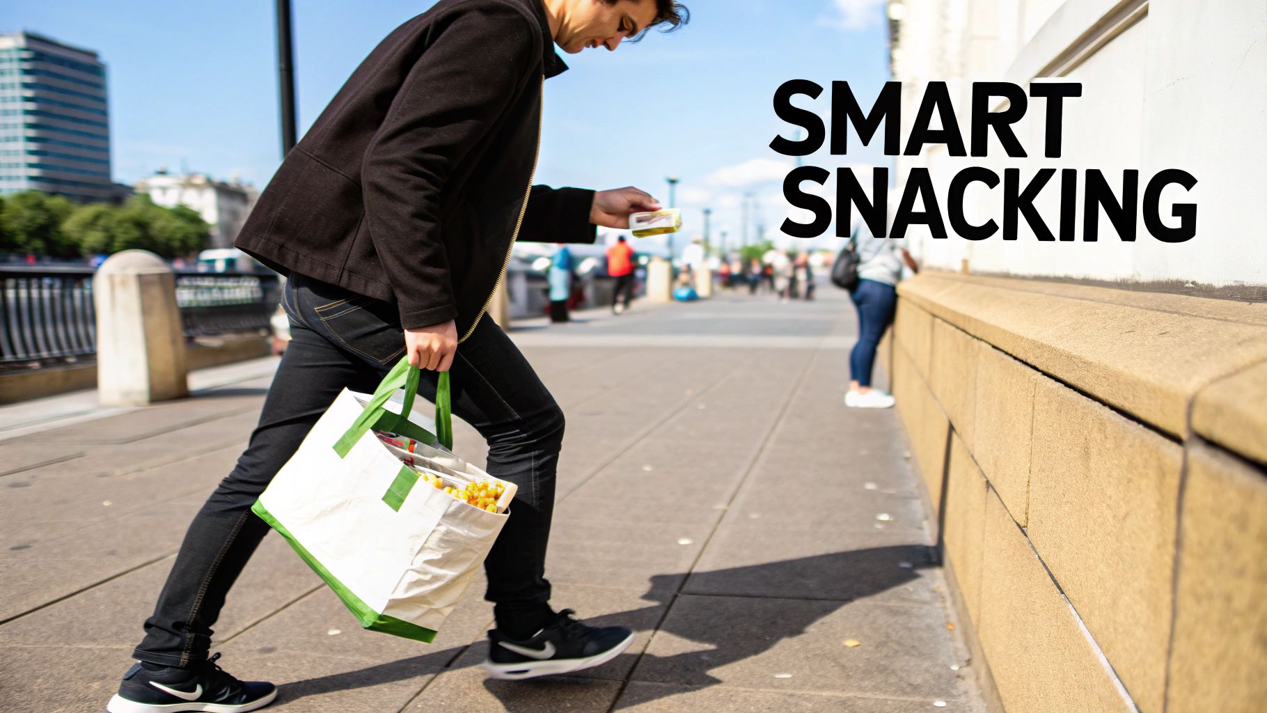 A person walks on a sunny city street, carrying a snack container and a reusable bag filled with snacks.