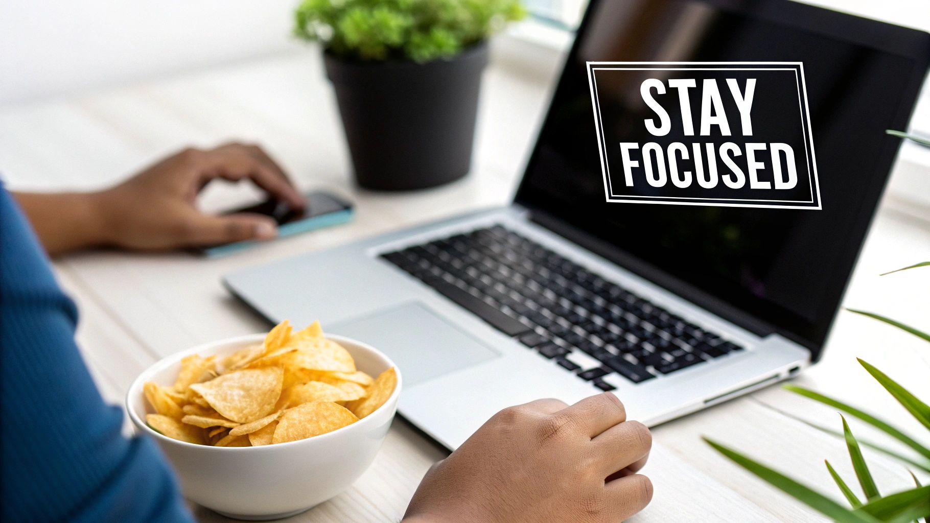 A person works on a laptop with "STAY FOCUSED" on screen, a bowl of chips nearby.