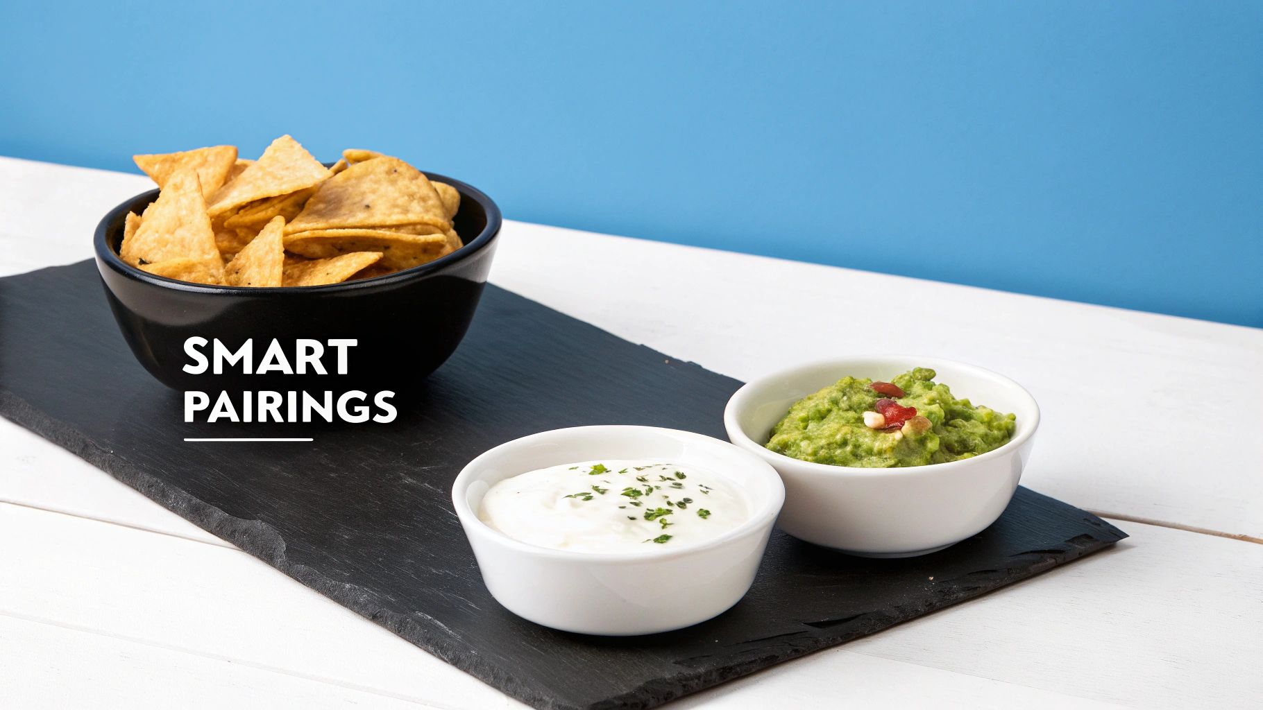 Tortilla chips, sour cream, and guacamole served as smart pairings on a black slate board.