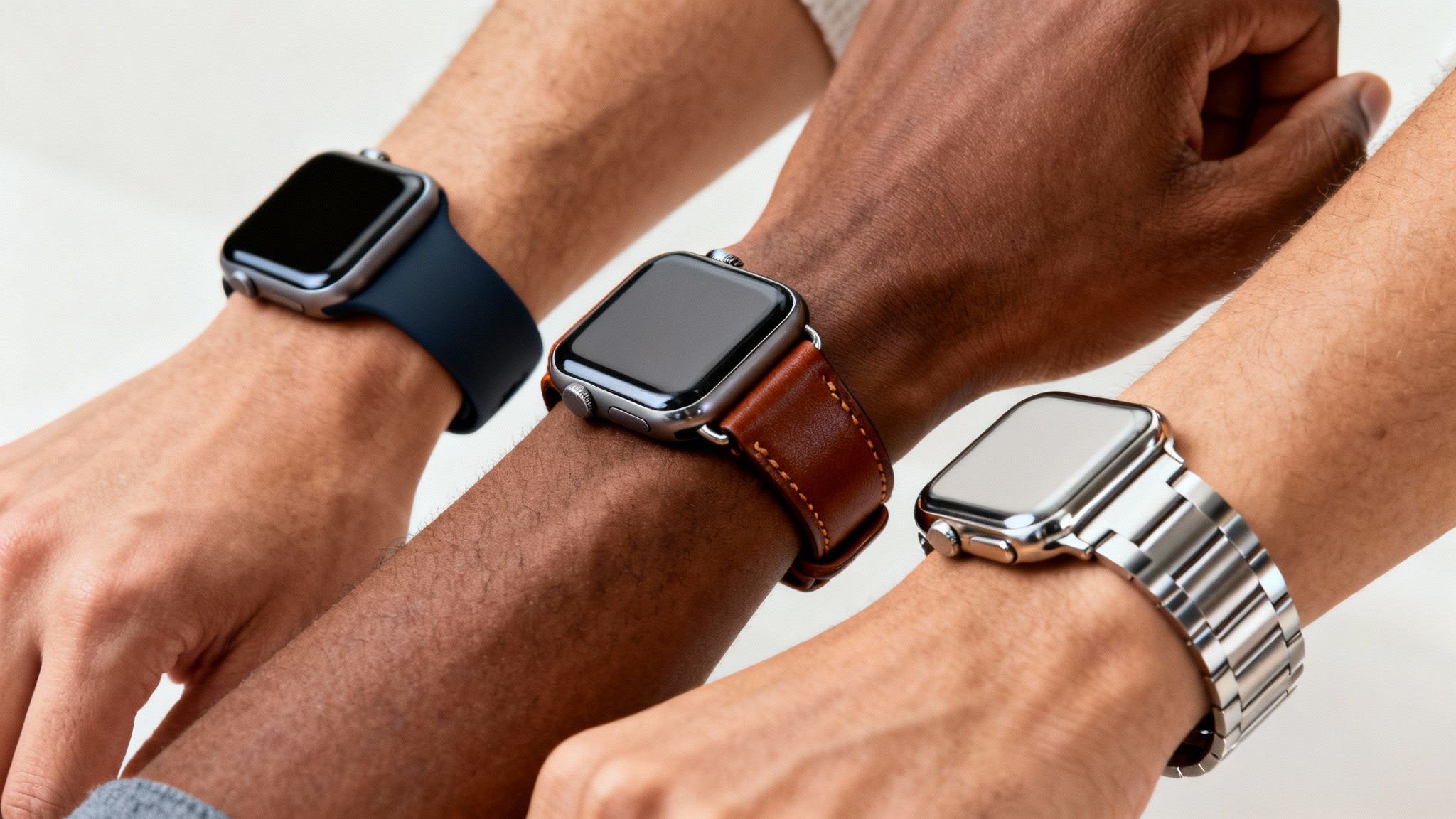 Three diverse arms wearing Apple Watches with different bands: blue, brown leather, and silver metal.