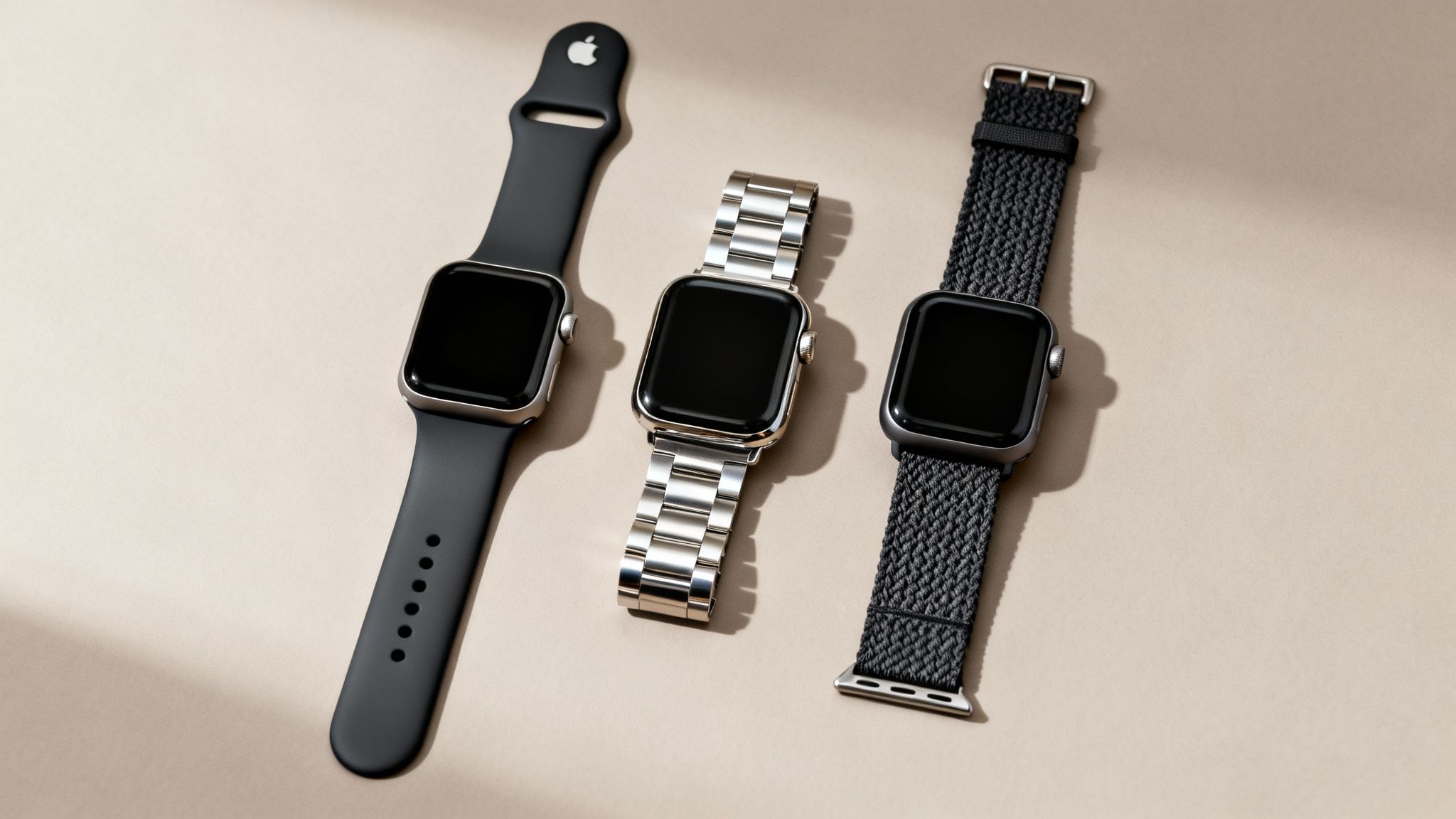 Three Apple Watches displayed with different bands: black silicone, silver metal link, and dark gray braided.