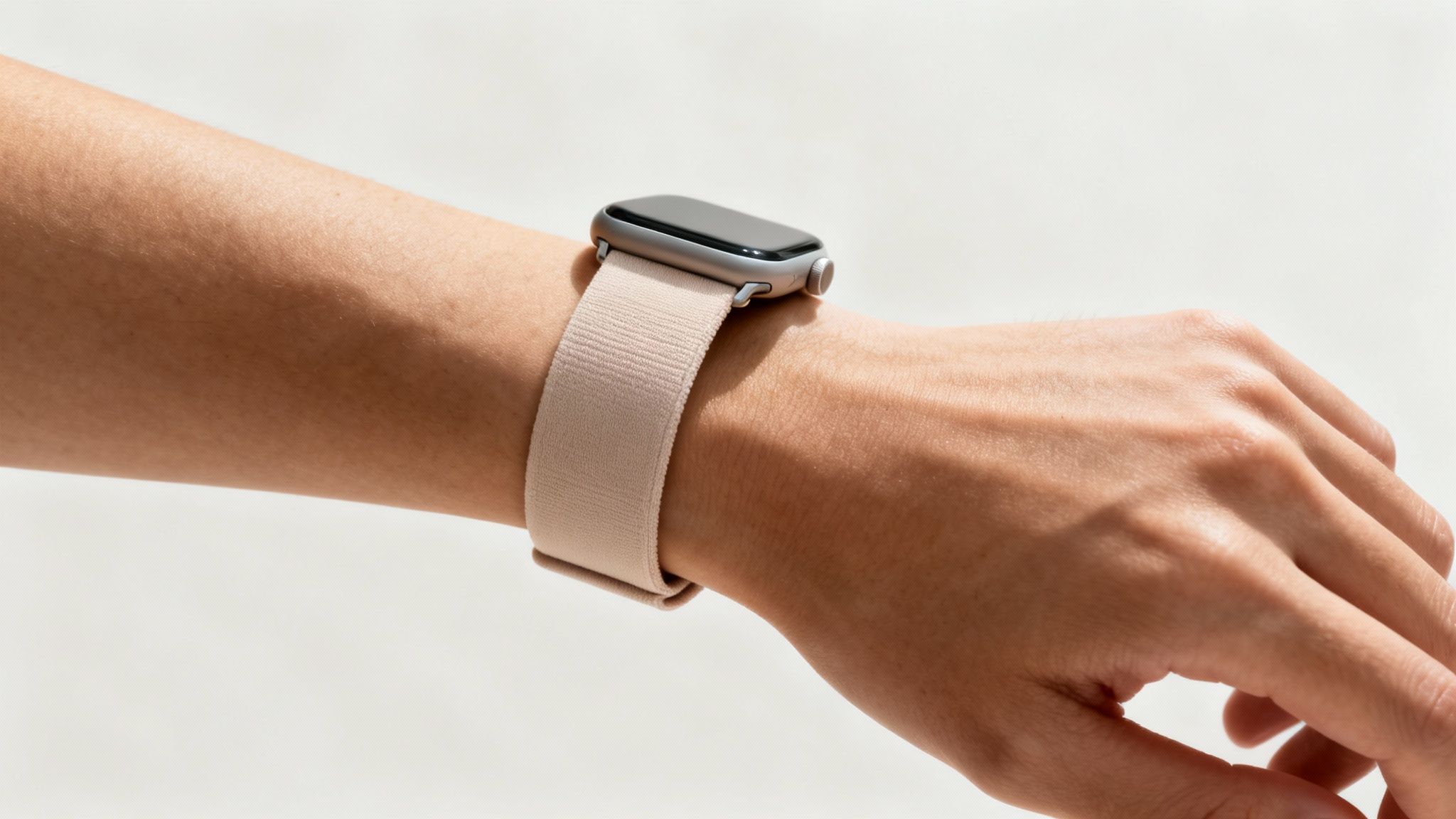 Close-up of a person's arm wearing a silver smart watch with a beige elasticated strap.