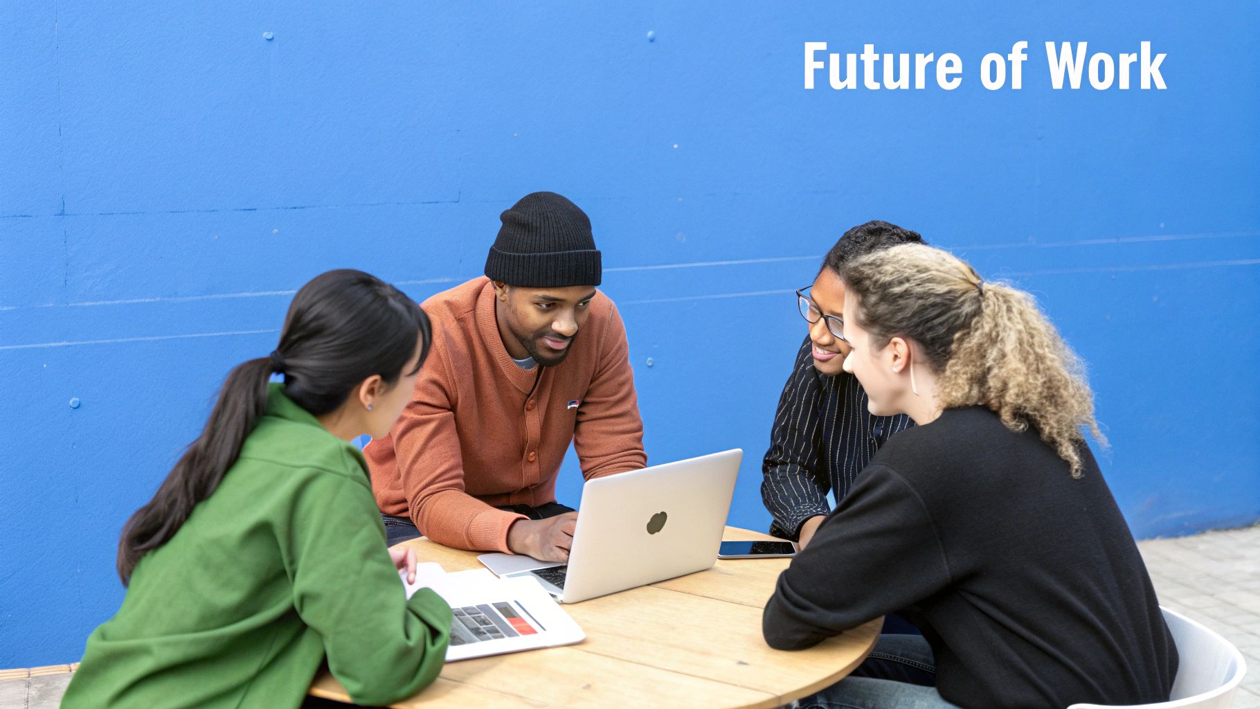Diverse young professionals collaborate on laptops at a wooden table with a blue background and 'Future of Work' text.