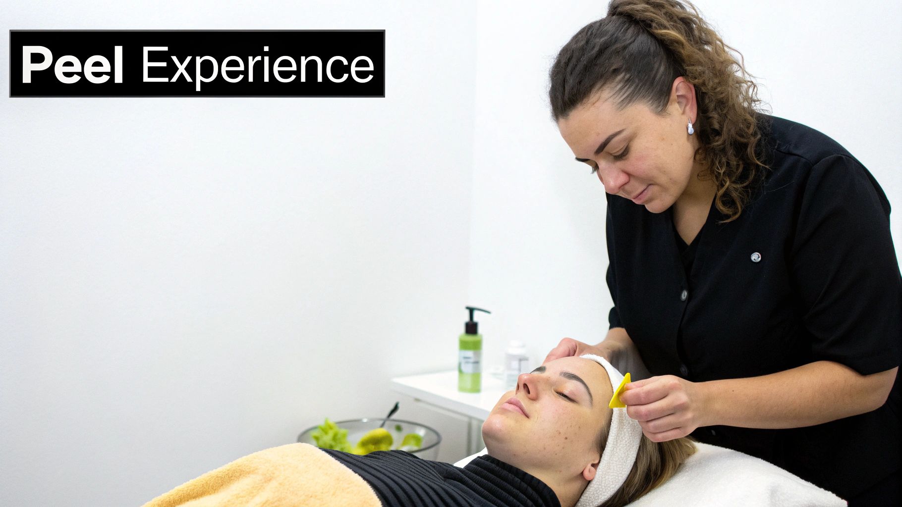 A woman receives a facial peel treatment from an aesthetician in a bright, clean spa setting.