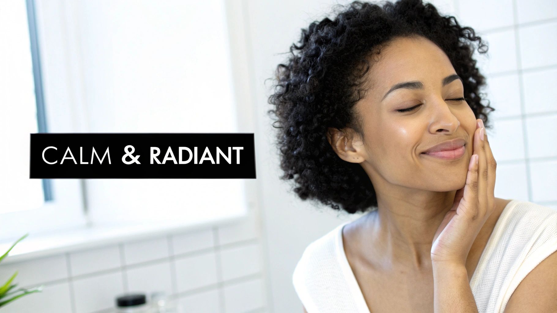 A calm, radiant woman with curly hair, eyes closed, gently touching her glowing skin.