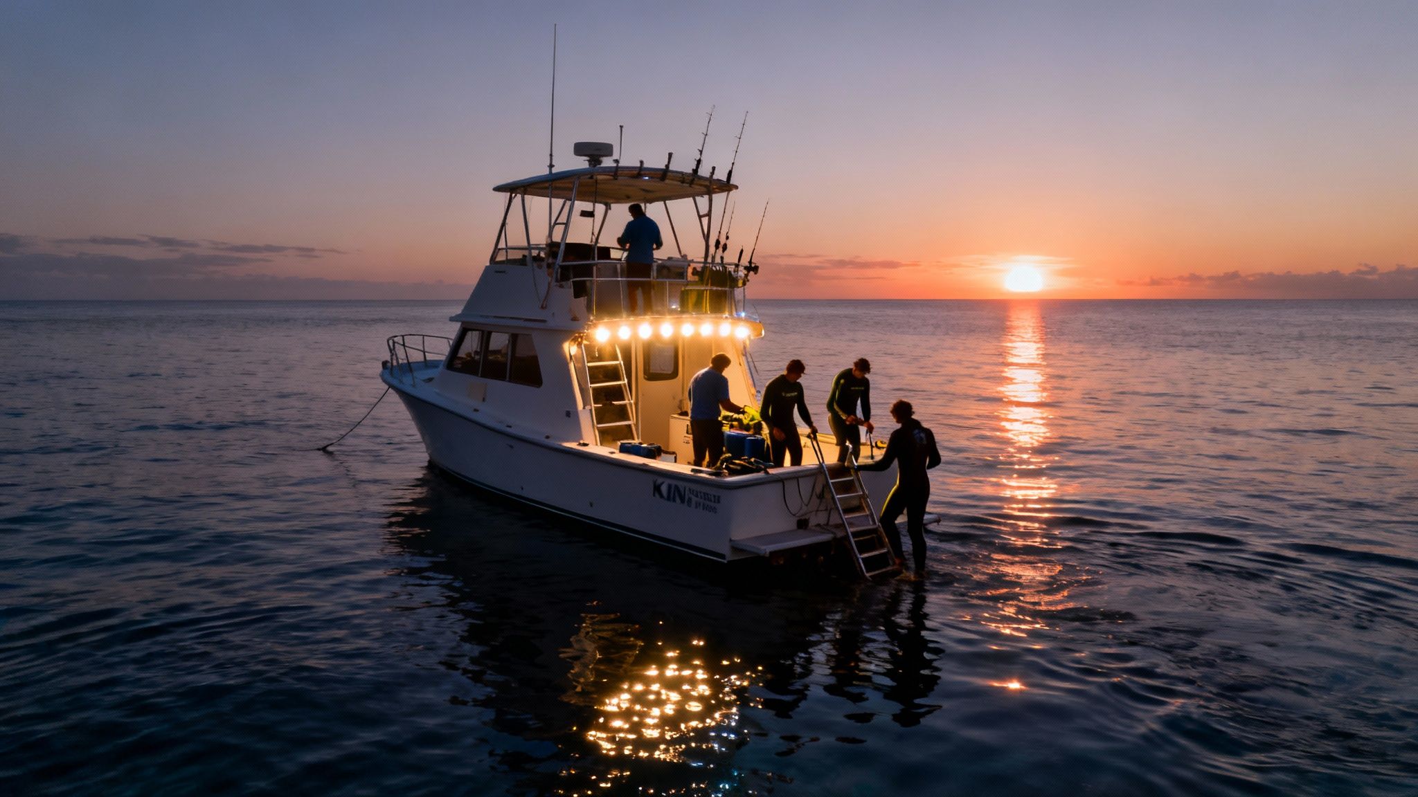 A boat with bright lights anchored at sunset, as divers prepare to enter the water.
