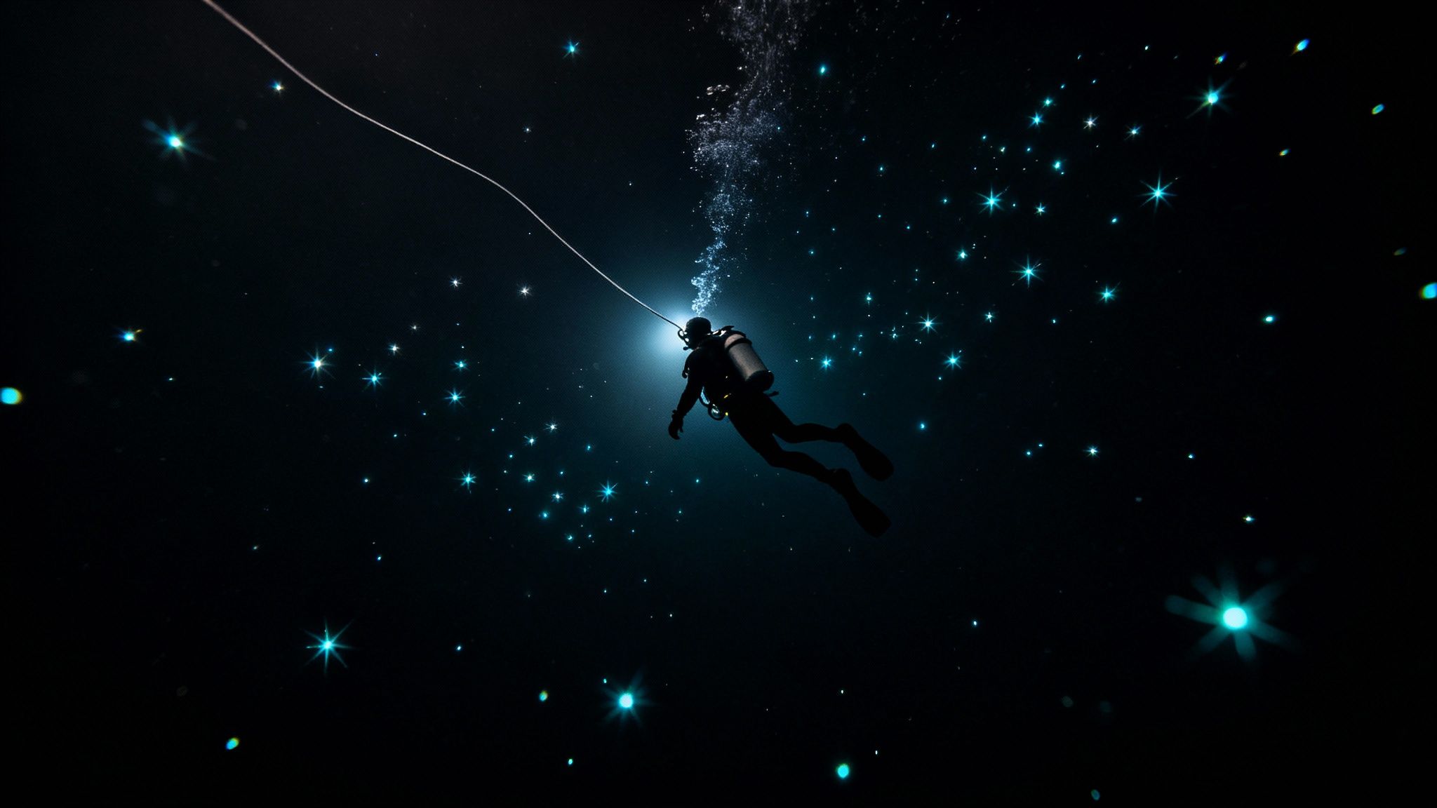 Scuba diver swimming underwater at night surrounded by bioluminescent plankton creating starry effect