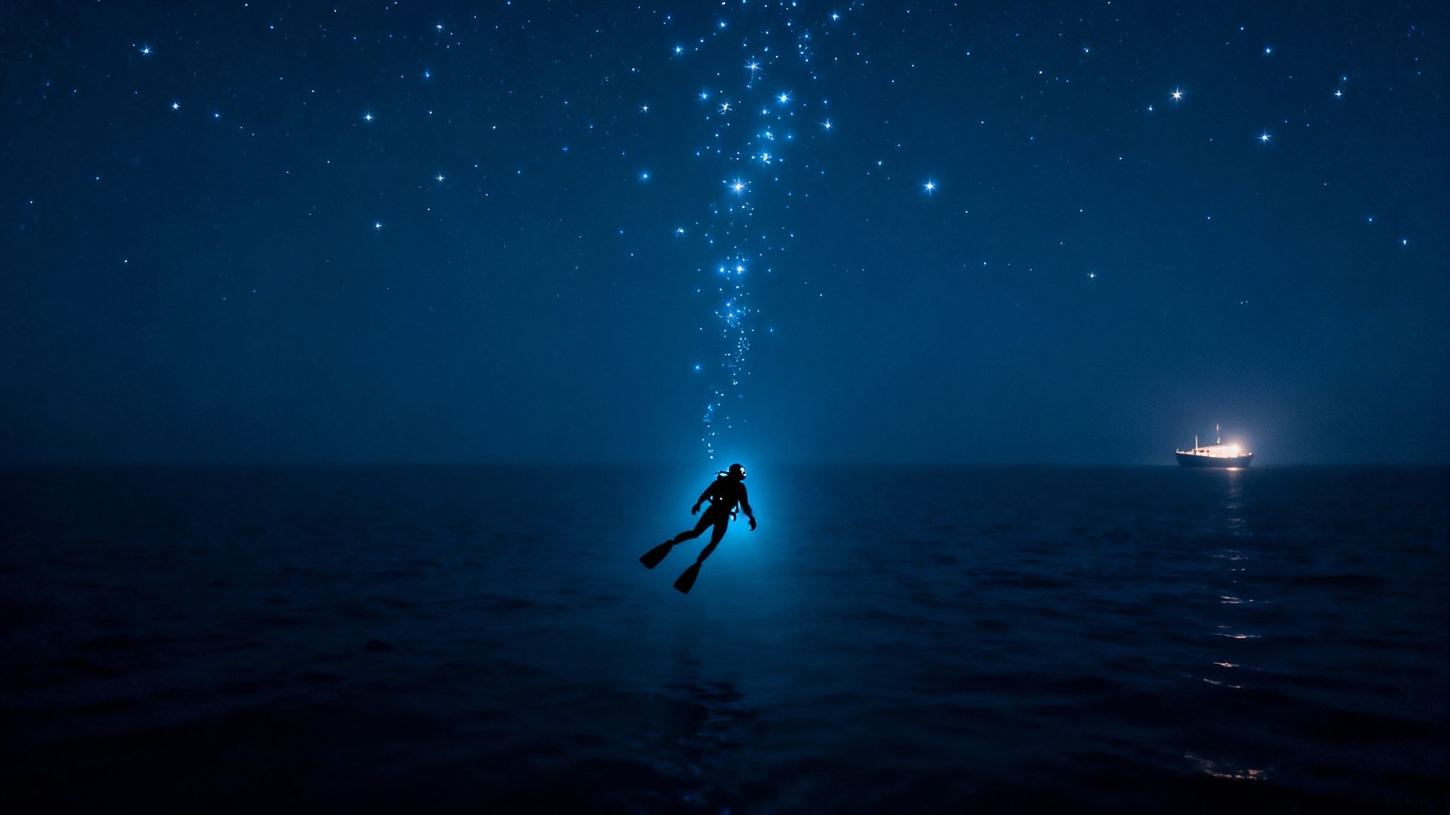 A diver ascends from deep blue water towards a starry night sky, illuminated by a celestial light path, with a ship in the distance.