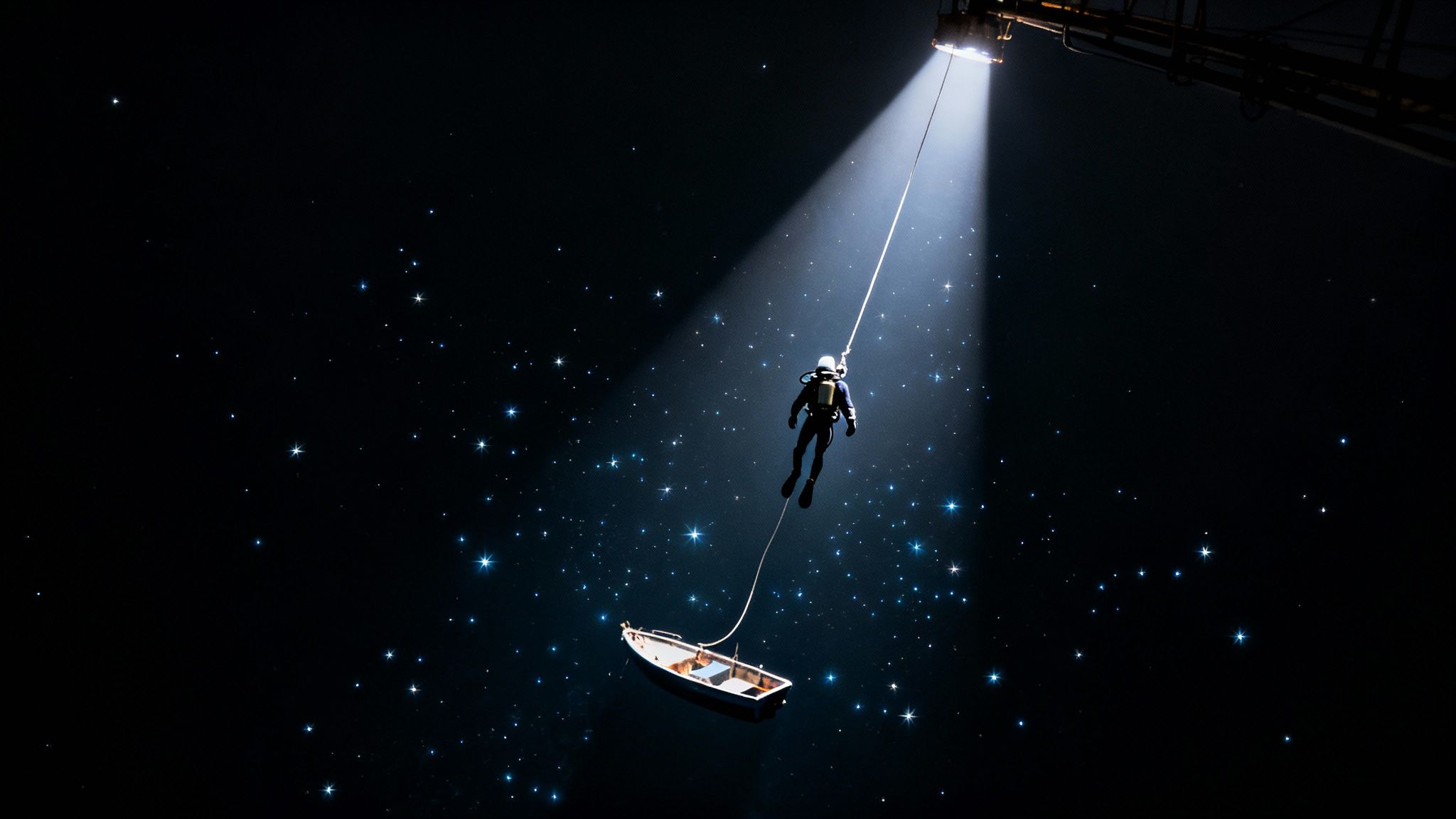 A diver descends from a spotlight into dark, star-filled water, pulling a small boat.