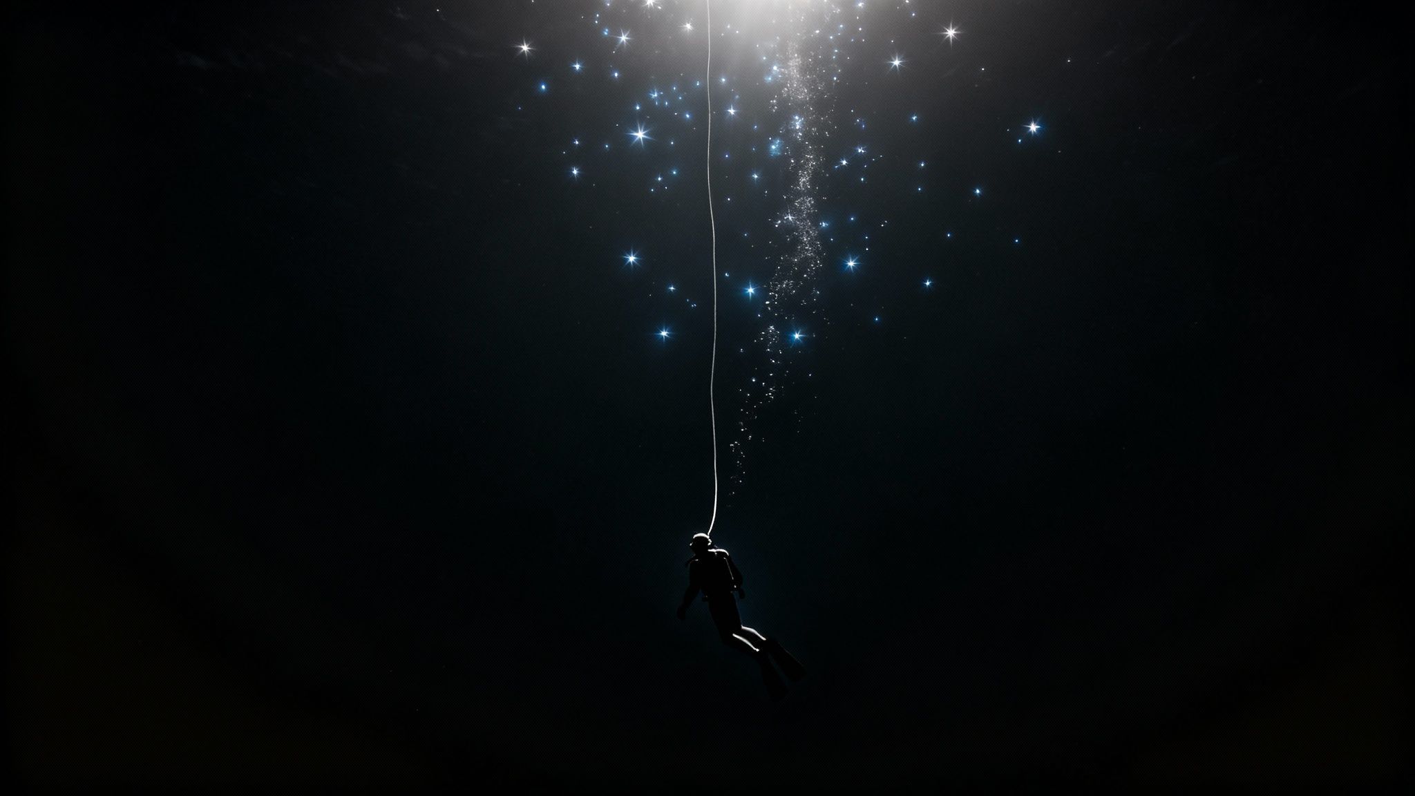 A silhouette of a freediver ascends from dark depths towards a starry, glowing water surface.