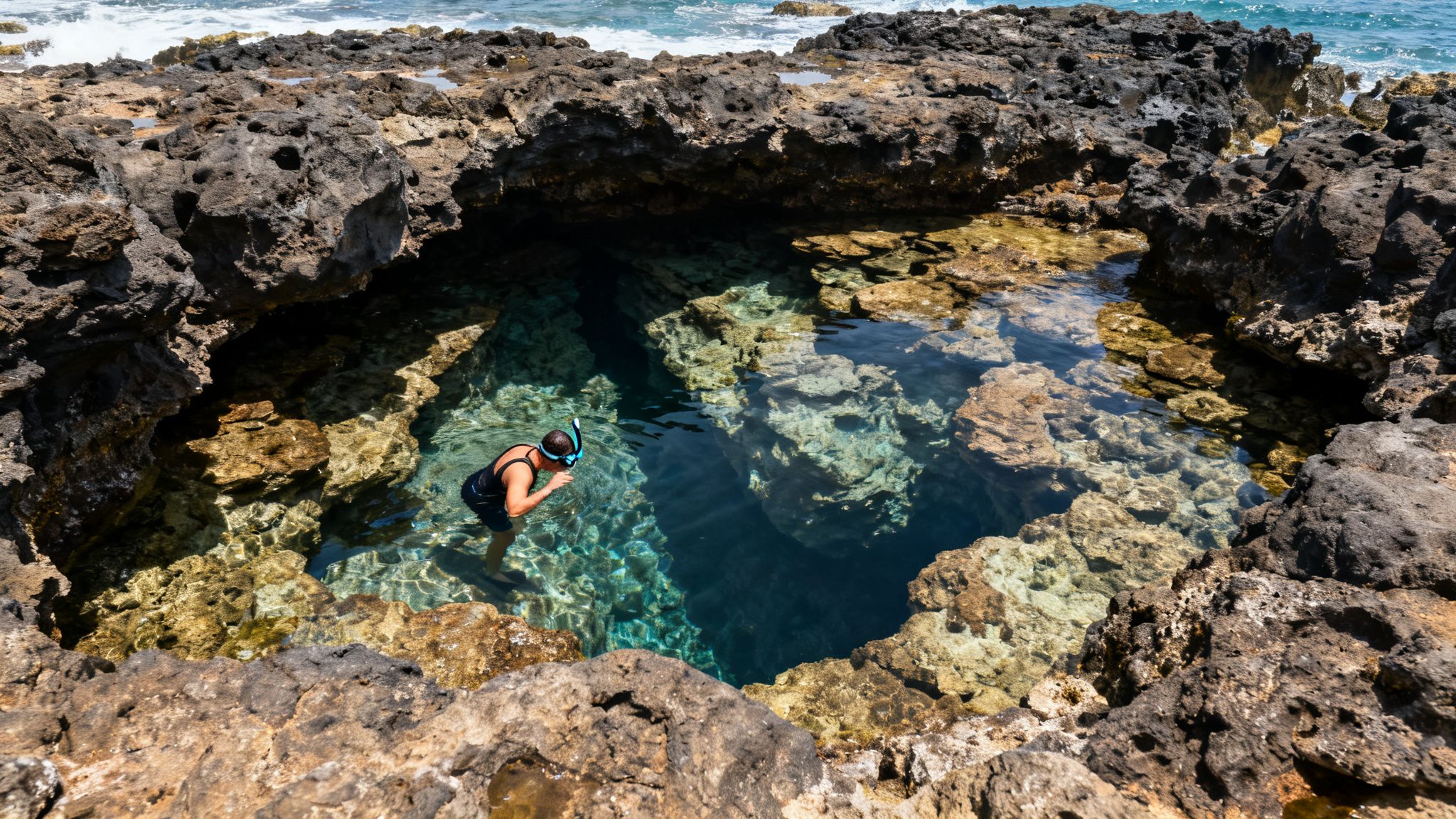 A person snorkeling in a clear natural tide pool surrounded by dark volcanic rocks with ocean in background.