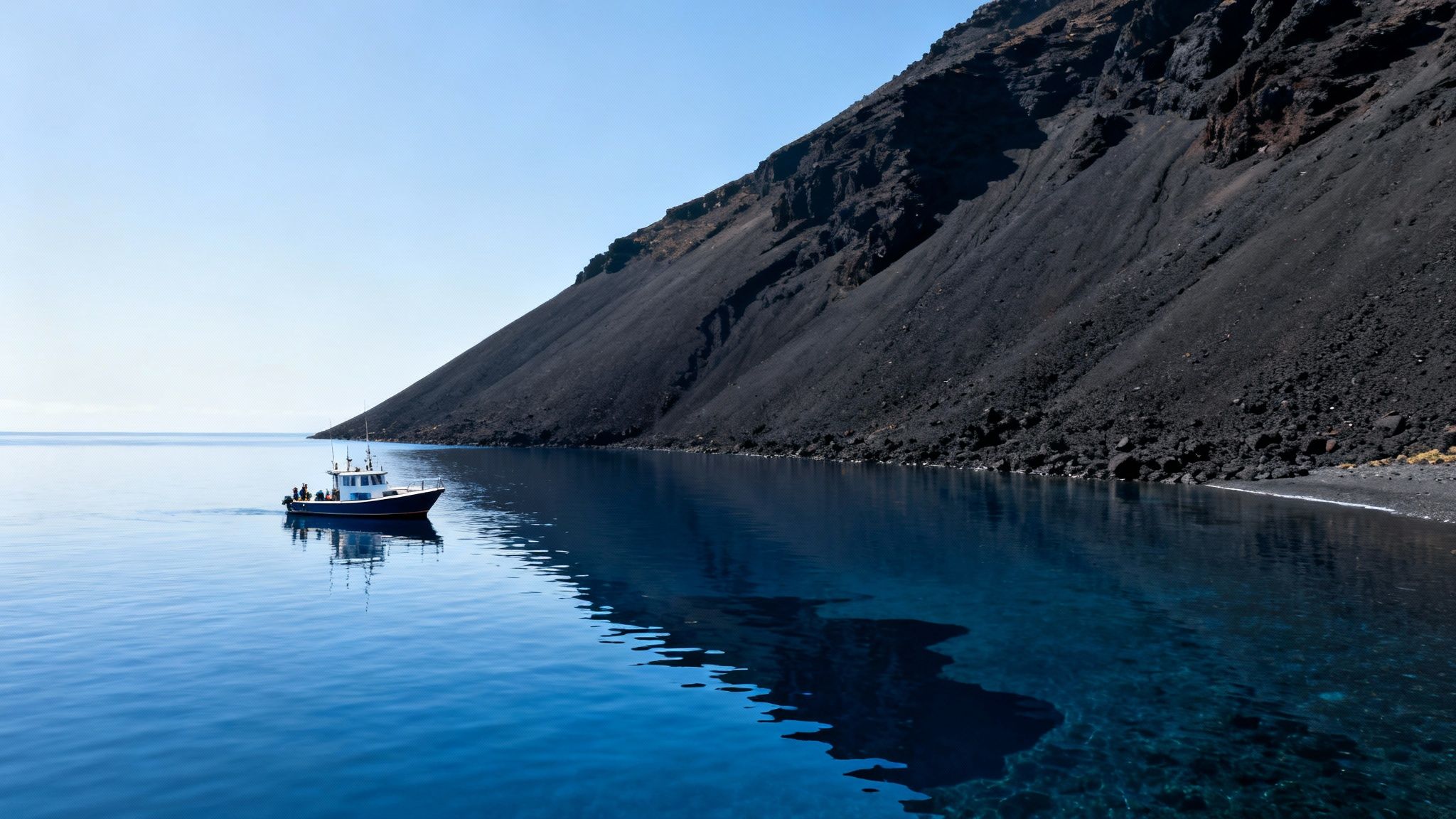 A small boat floats on serene blue water beside a steep black volcanic mountain under a clear sky.