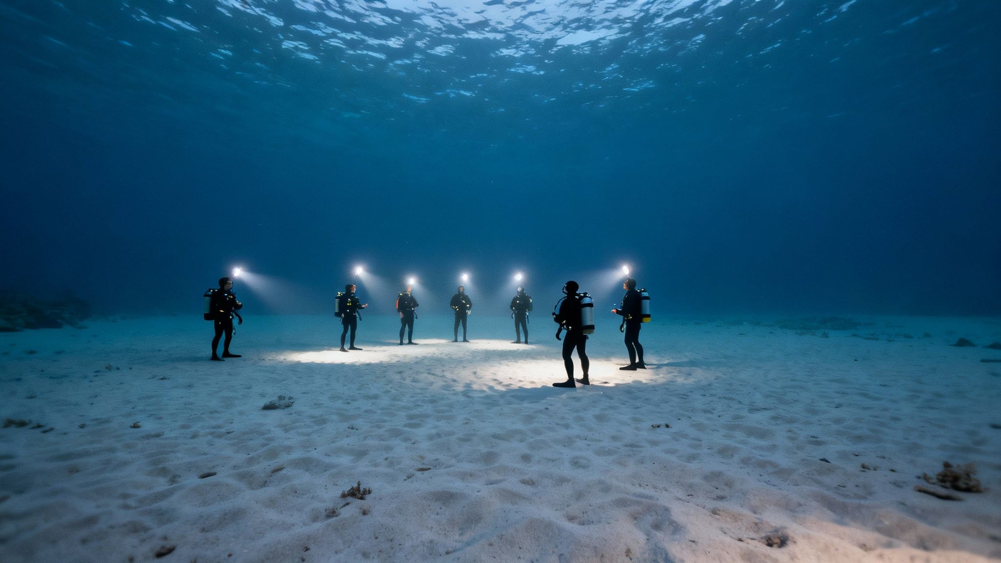 A manta ray glides just above a scuba diver, who is shining their light upwards.