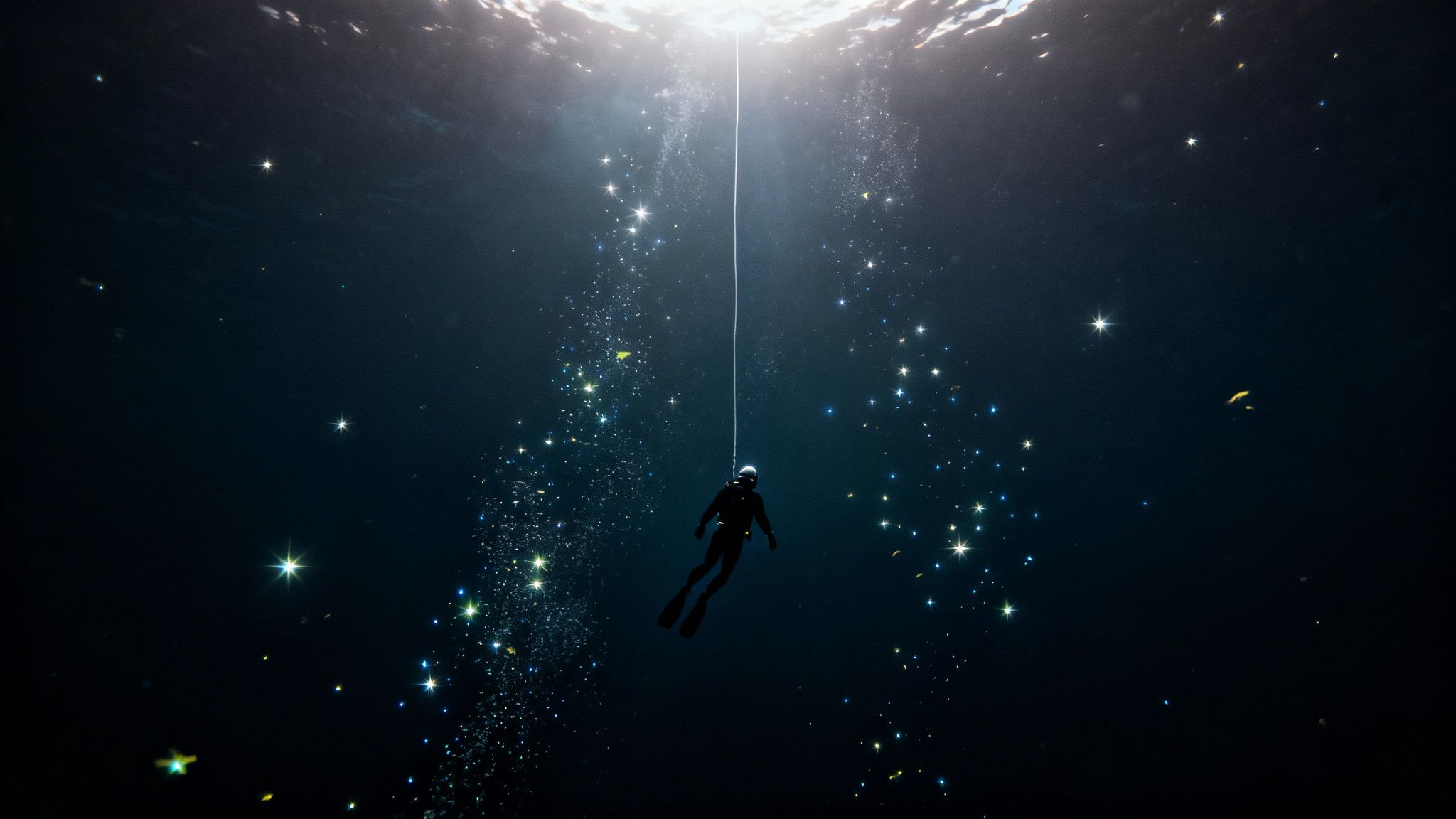 A diver is suspended by a rope deep underwater, surrounded by sparkling light resembling stars.