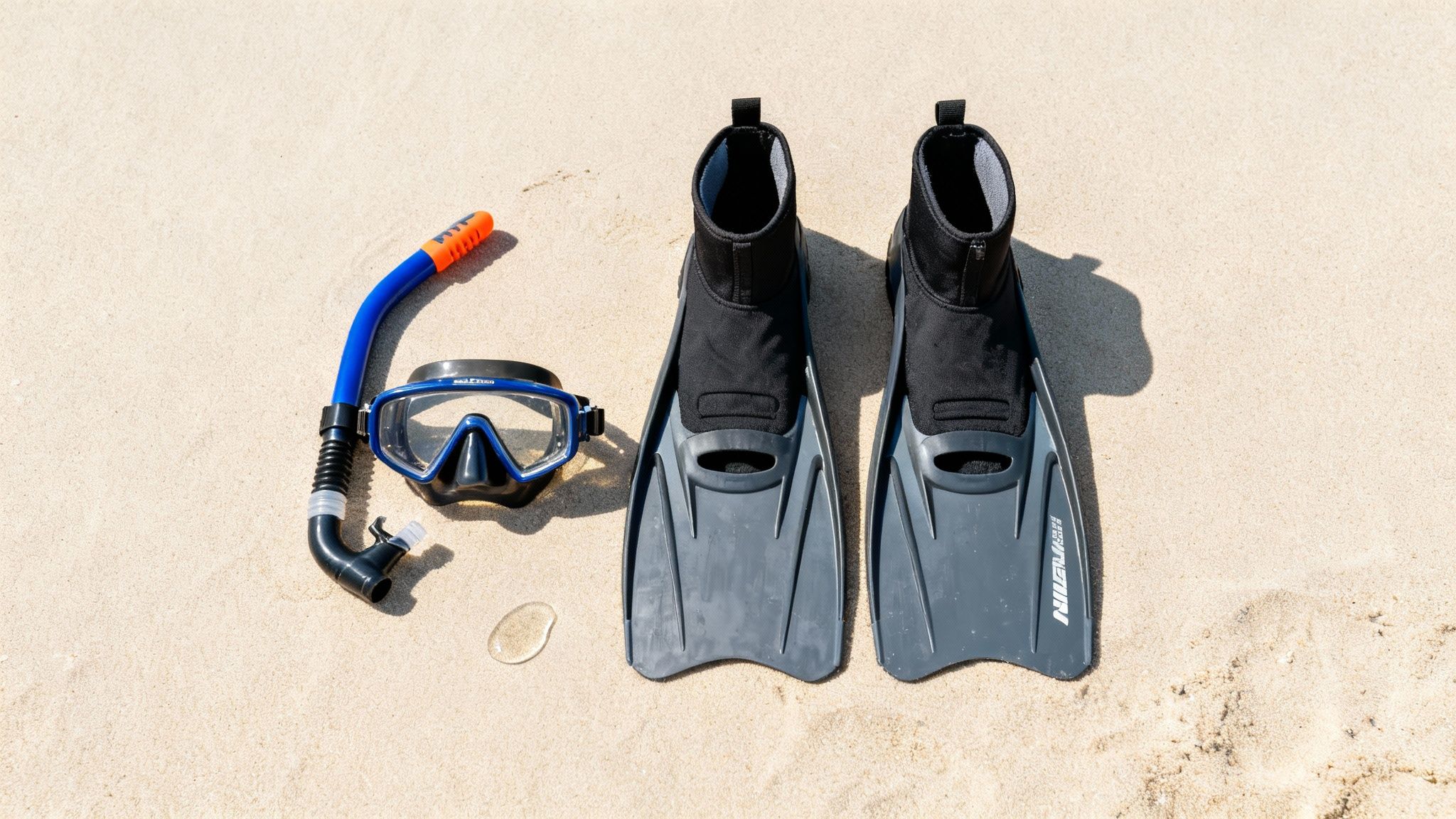 Snorkeling gear including a blue mask, snorkel, and black fins laid on a sandy beach.
