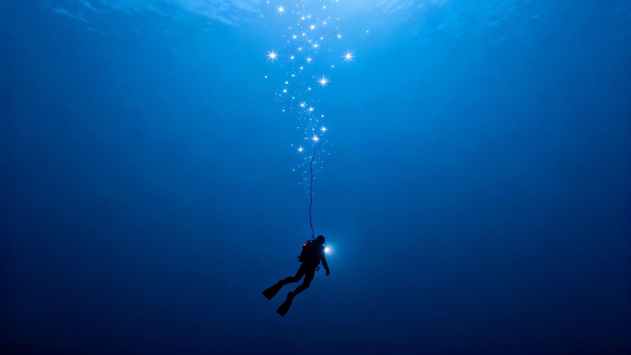 A scuba diver illuminates a dark, deep-water scene with a flashlight during an advanced dive off the Big Island.