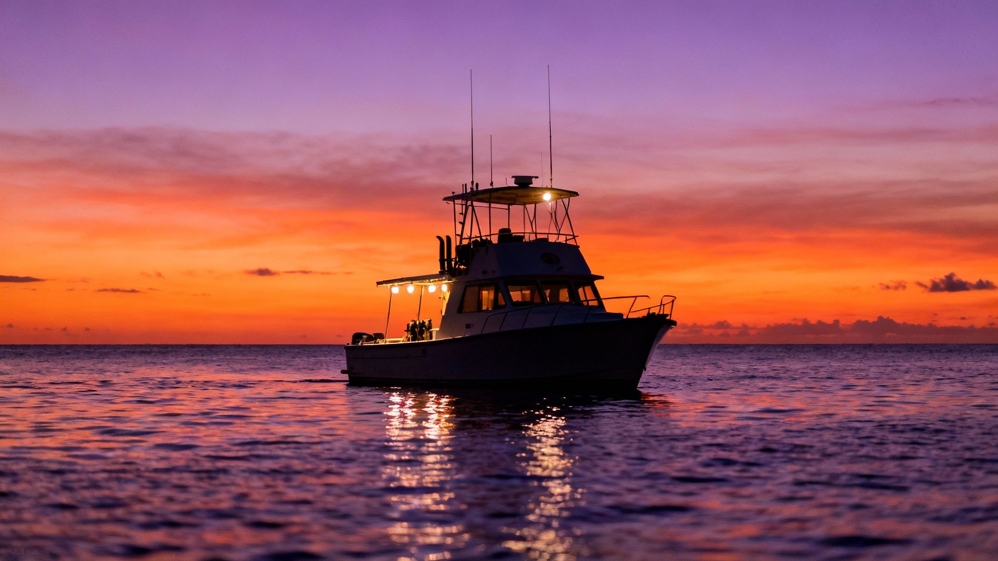 A group of scuba divers on the ocean floor watching a manta ray swim overhead.