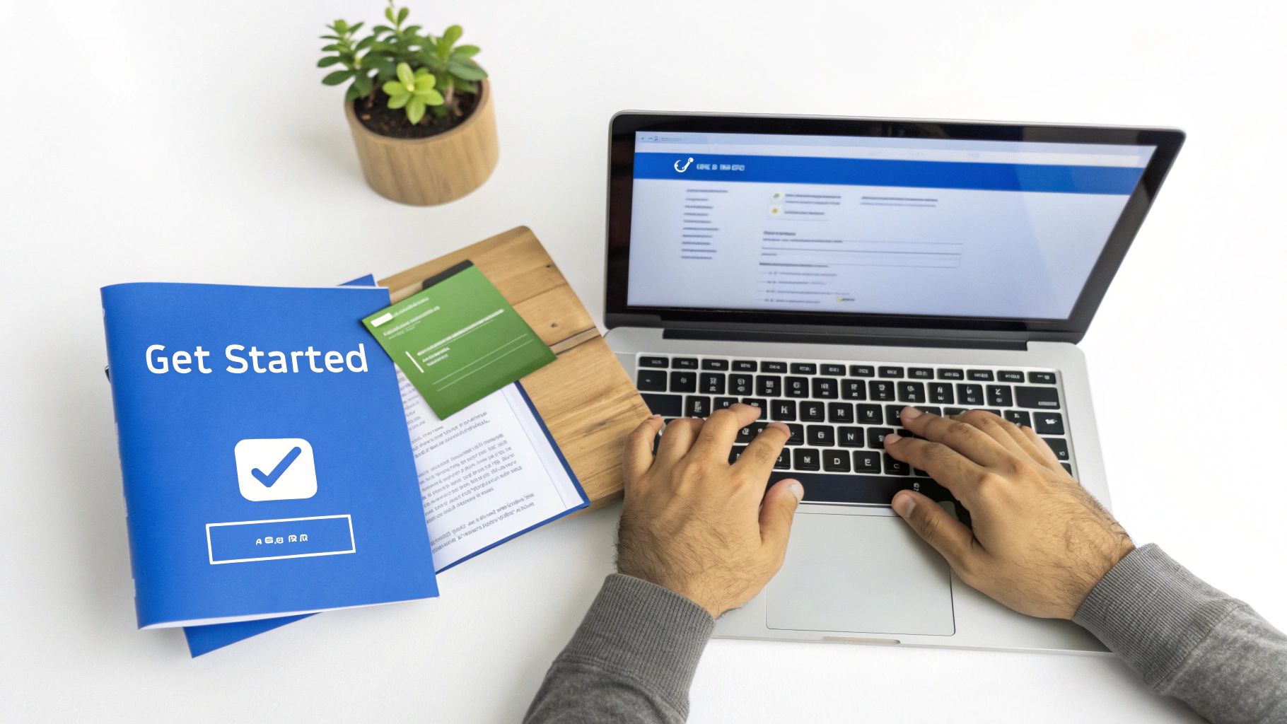 Overhead view of a person typing on a laptop next to a 'Get Started' book and a plant.