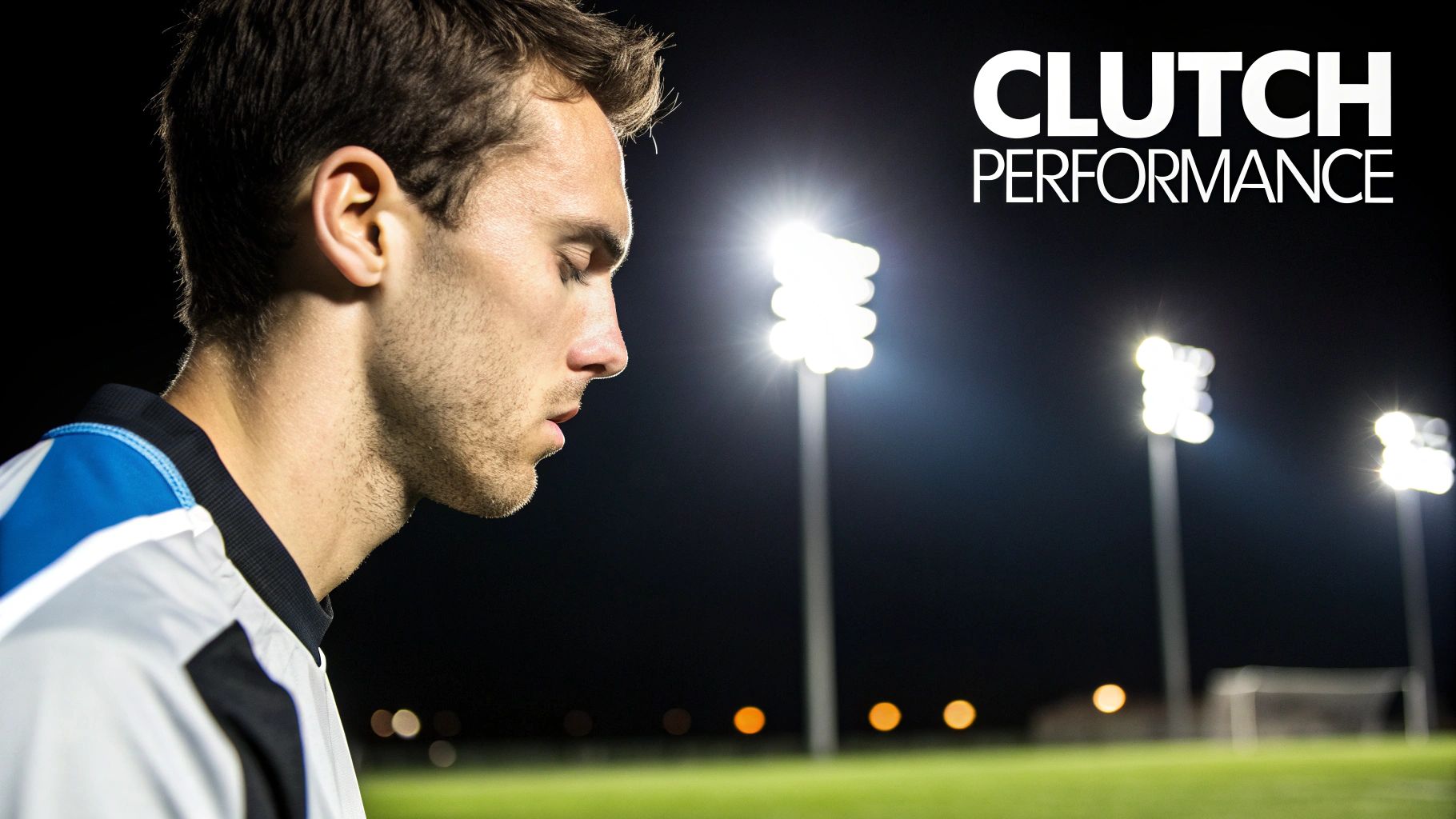 A male soccer player, head down in thought, on a floodlit field at night.