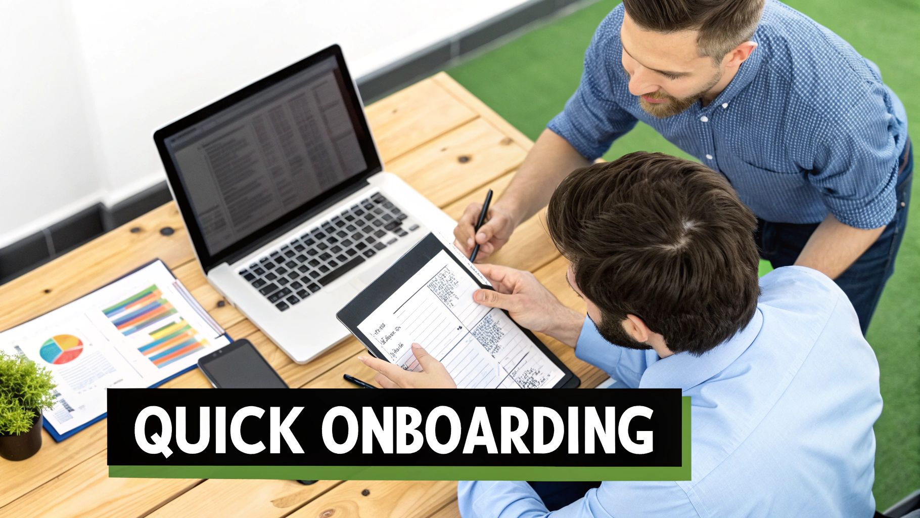 Overhead view of two men discussing on a tablet during a quick onboarding session at a desk.