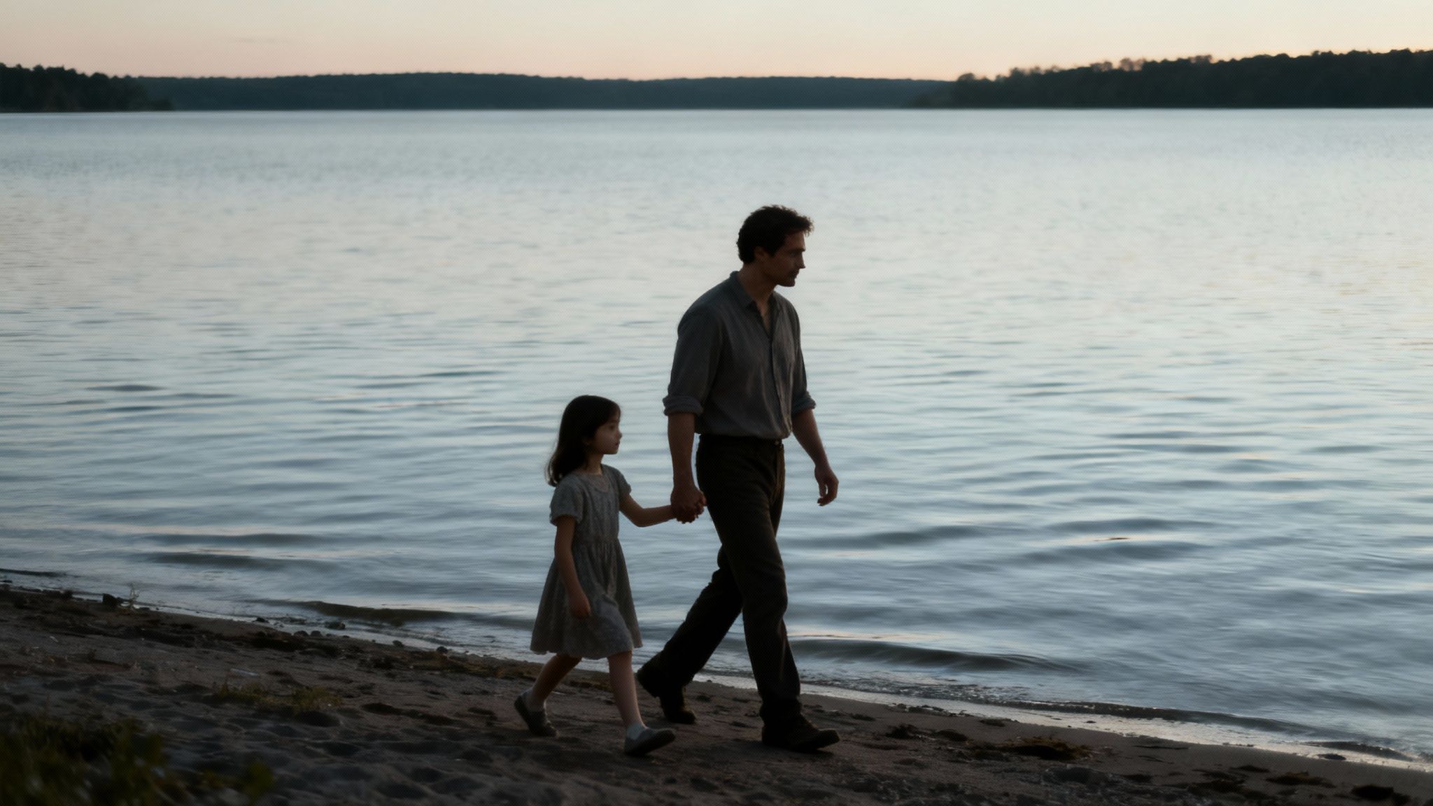 A father and young daughter hold hands, walking along a sandy lake shore at dusk.