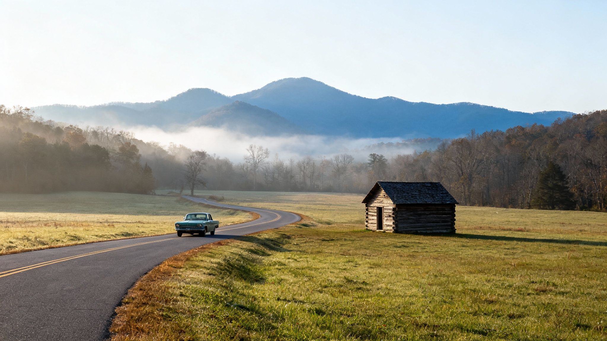 A vintage car drives on a winding road past a rustic cabin in a misty mountain valley.