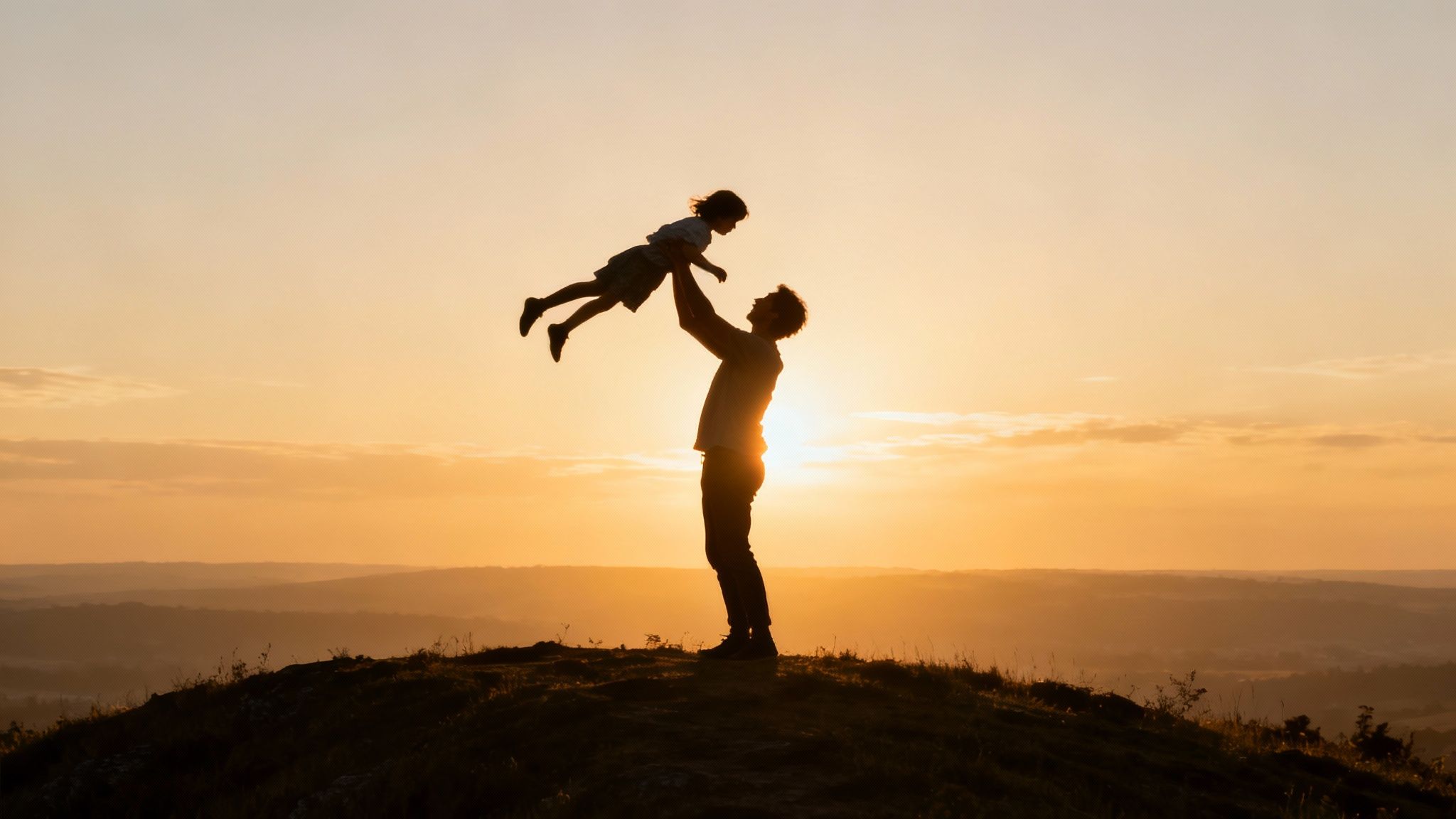 Father lifting child in air during golden sunset on hilltop silhouette