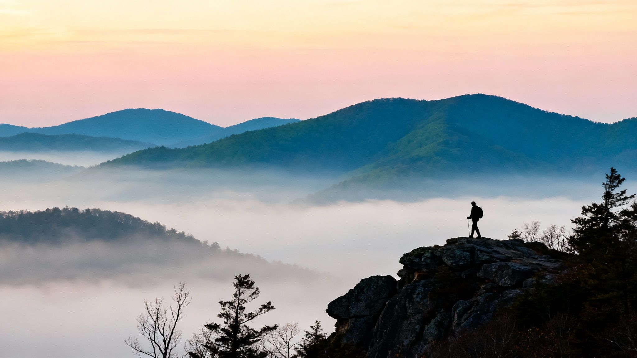 A lone hiker stands on a mountain cliff, overlooking a misty valley at sunrise.