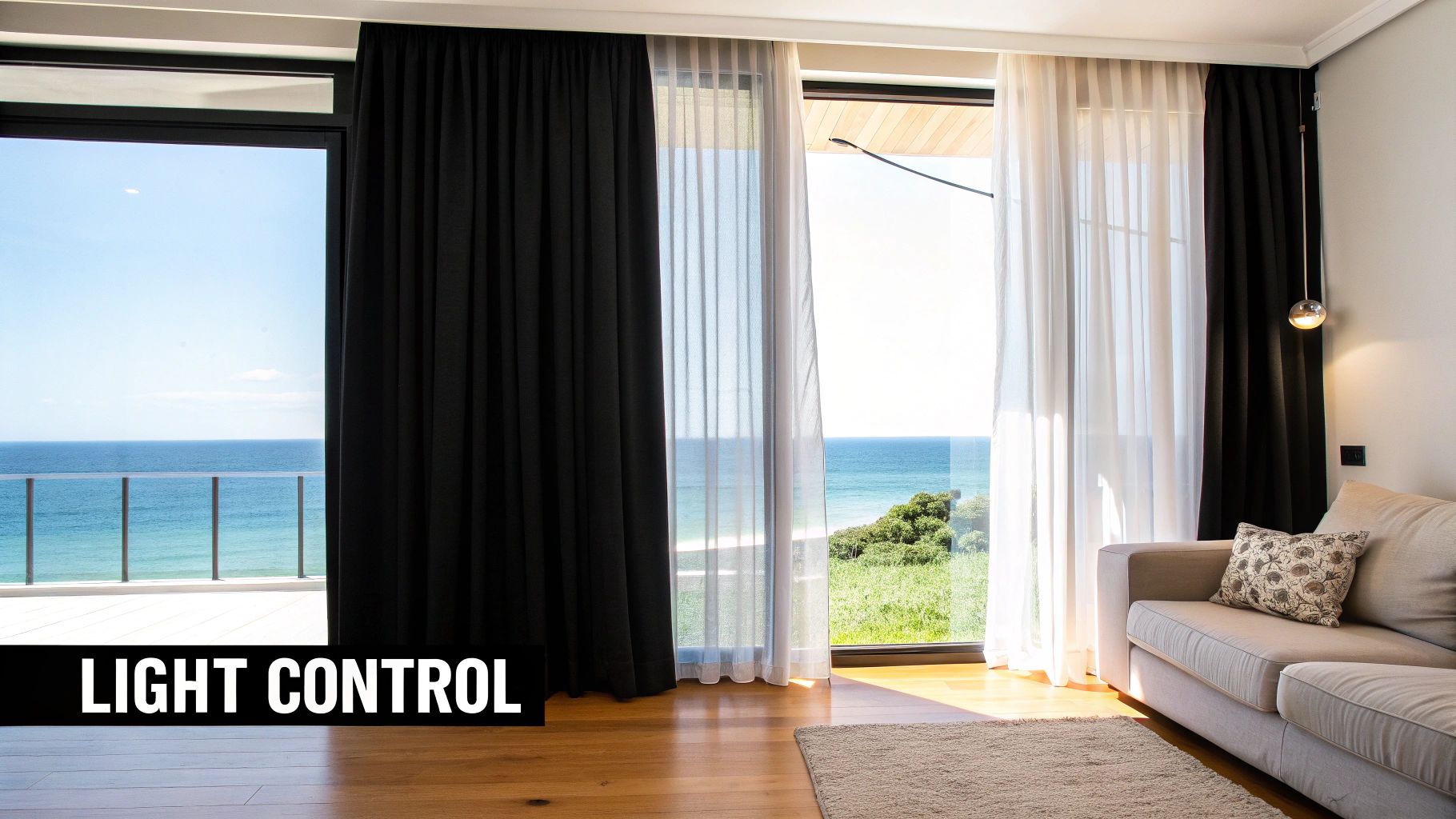 A modern room with black and sheer white curtains, a beige couch, and an ocean view.
