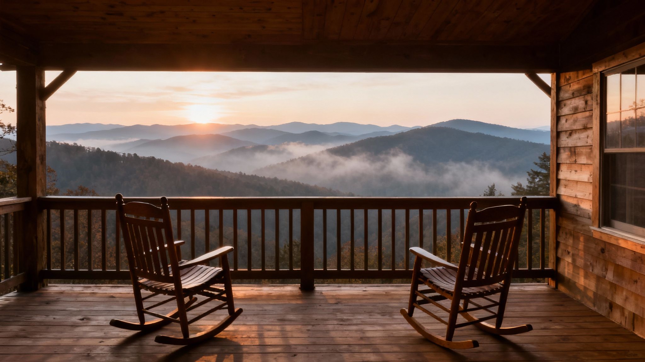 Two wooden rocking chairs on a rustic cabin porch overlooking misty mountains at sunrise.