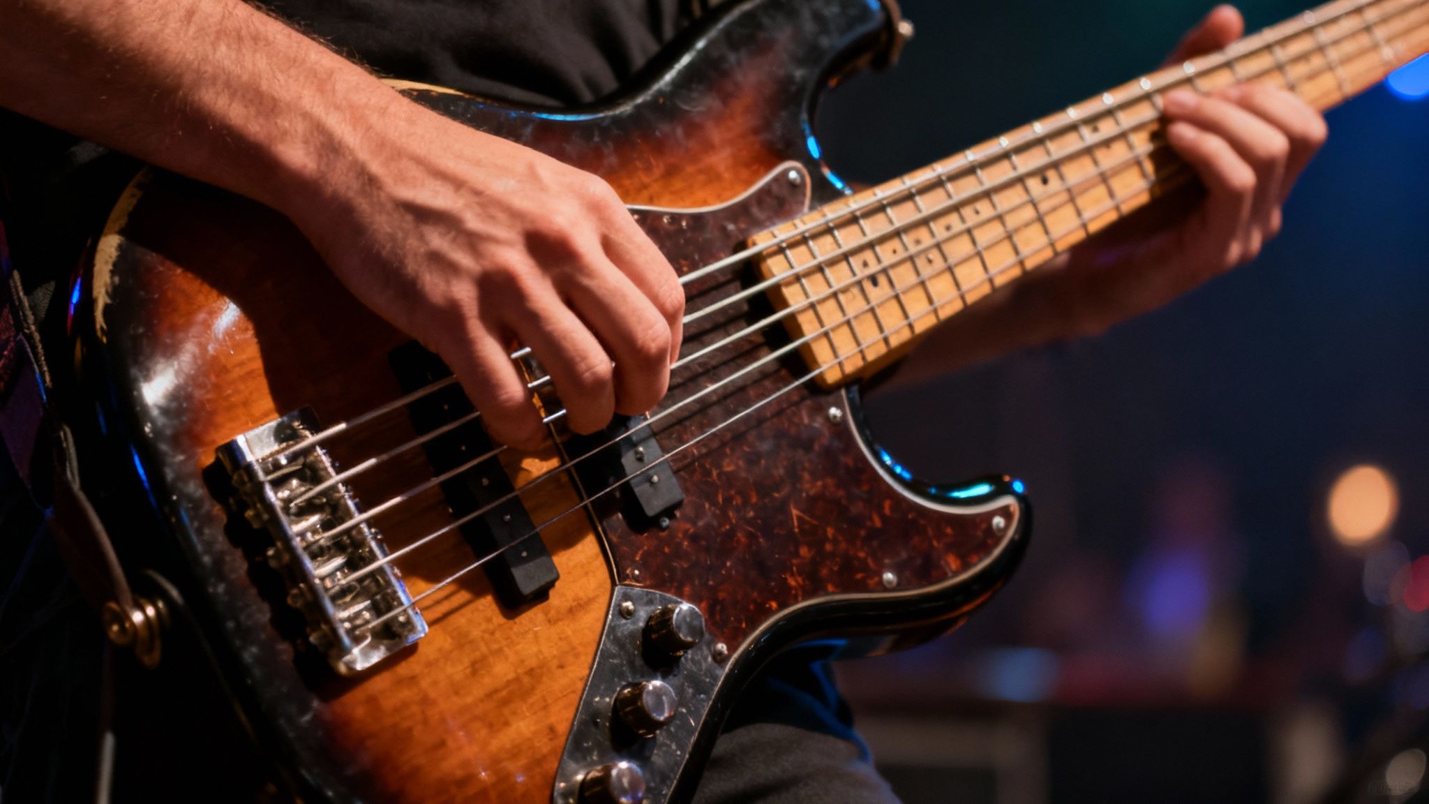 Bass guitarist playing worn sunburst electric bass guitar during live band performance on stage