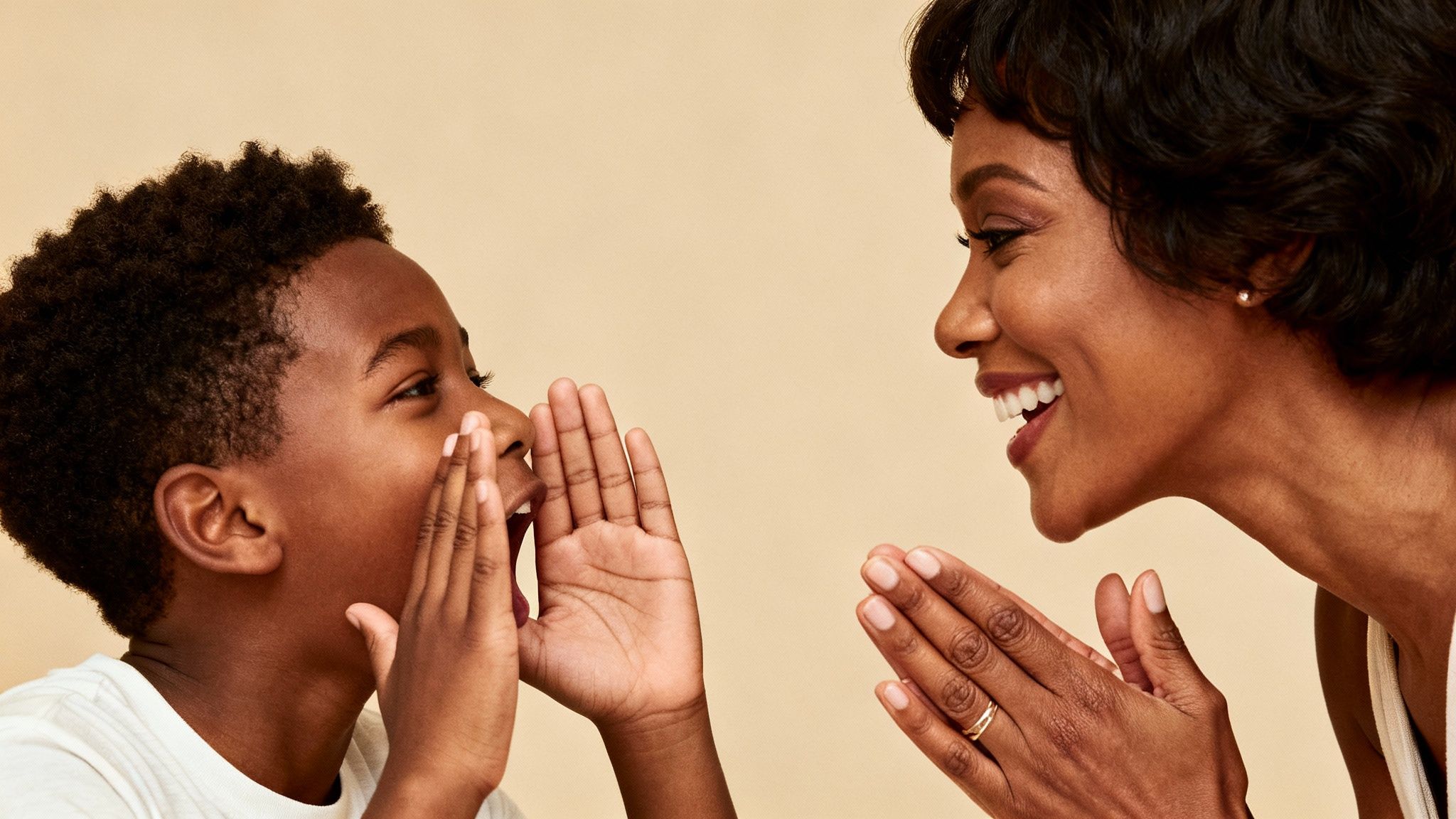 A joyful African American boy whispers a secret to his smiling mother, sharing a happy moment.