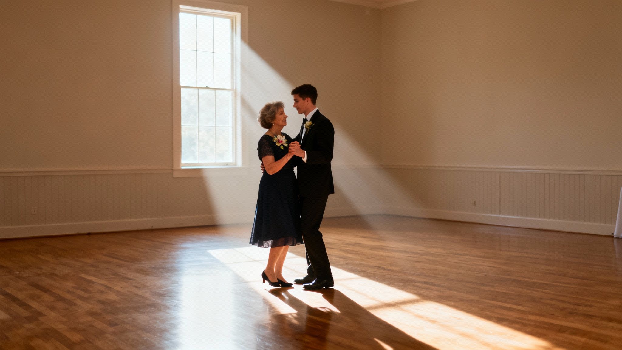 A mother and son smiling while dancing in a sunlit room with wooden floors, celebrating a special moment.