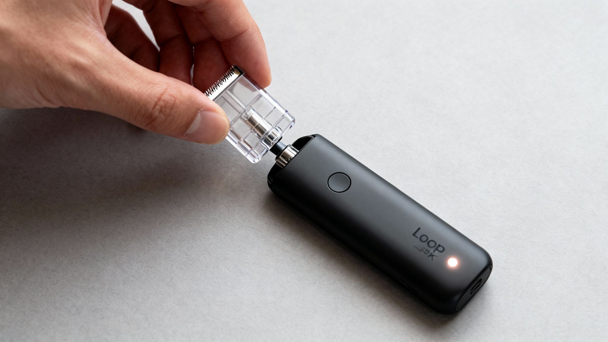 A hand inserts a clear pod into a black Loop vaping device with a glowing light.
